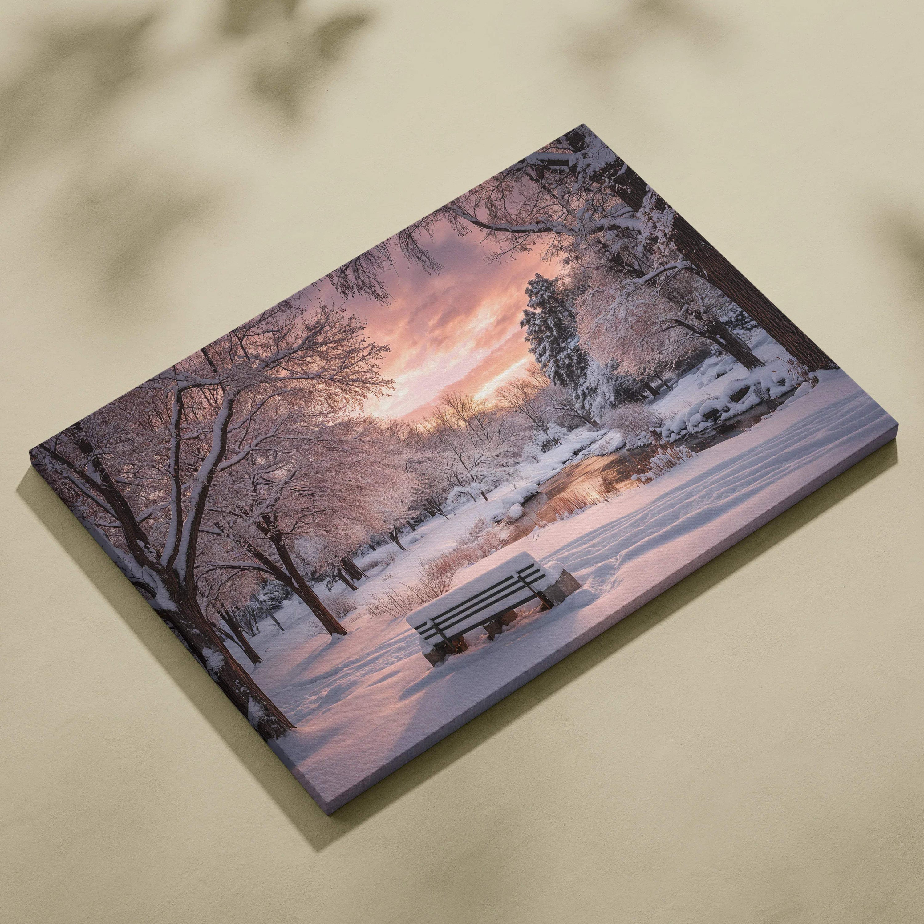Snowy park bench by stream under pink orange dusk sky canvas art