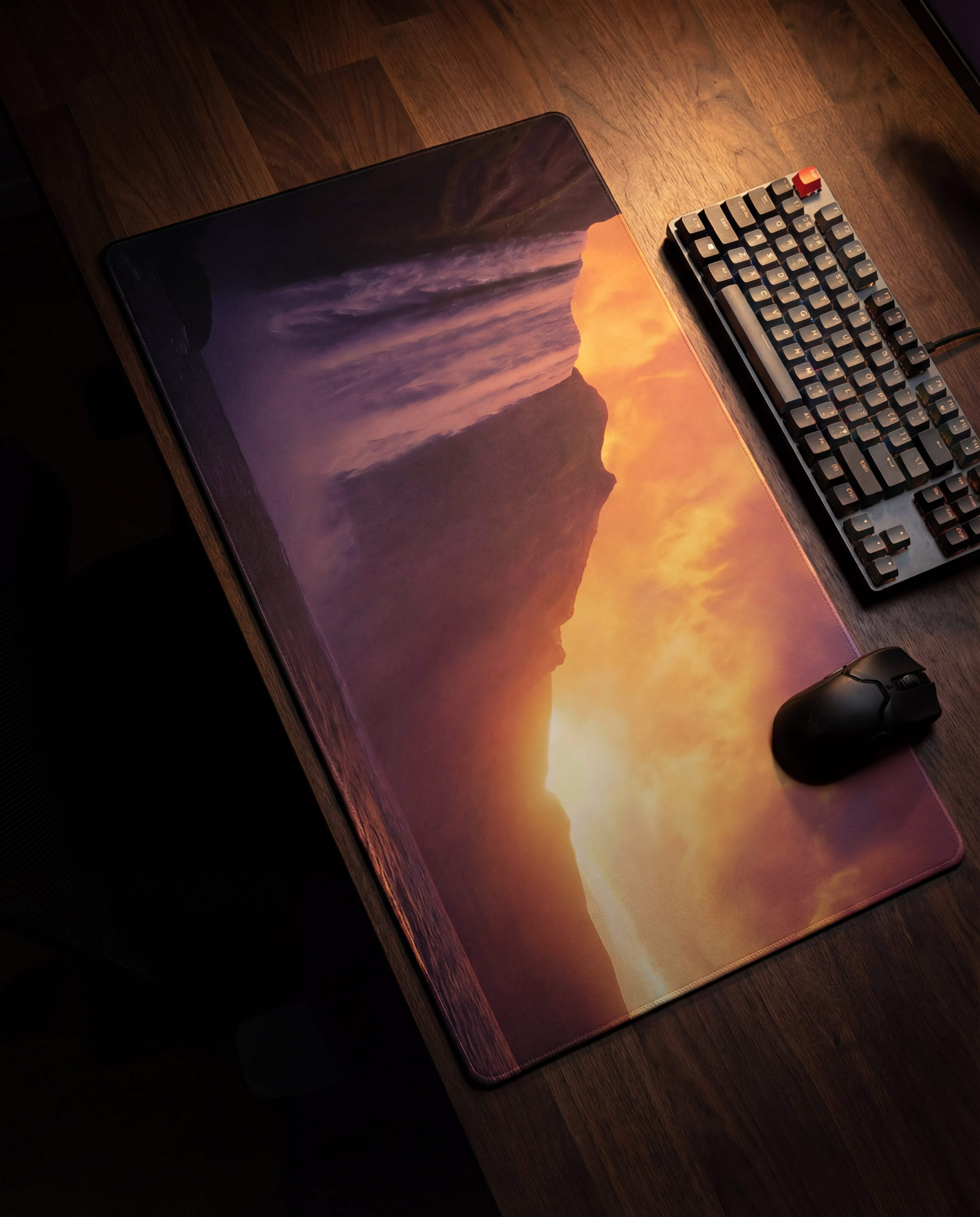 A rectangular gaming mousepad featuring a vivid sunset cliffside scene with warm orange and purple hues, printed on a smooth surface.