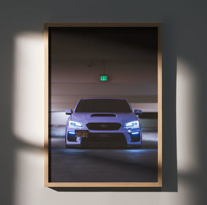 Framed Subaru WRX poster wall art with blue headlights in a dimly lit parking garage.