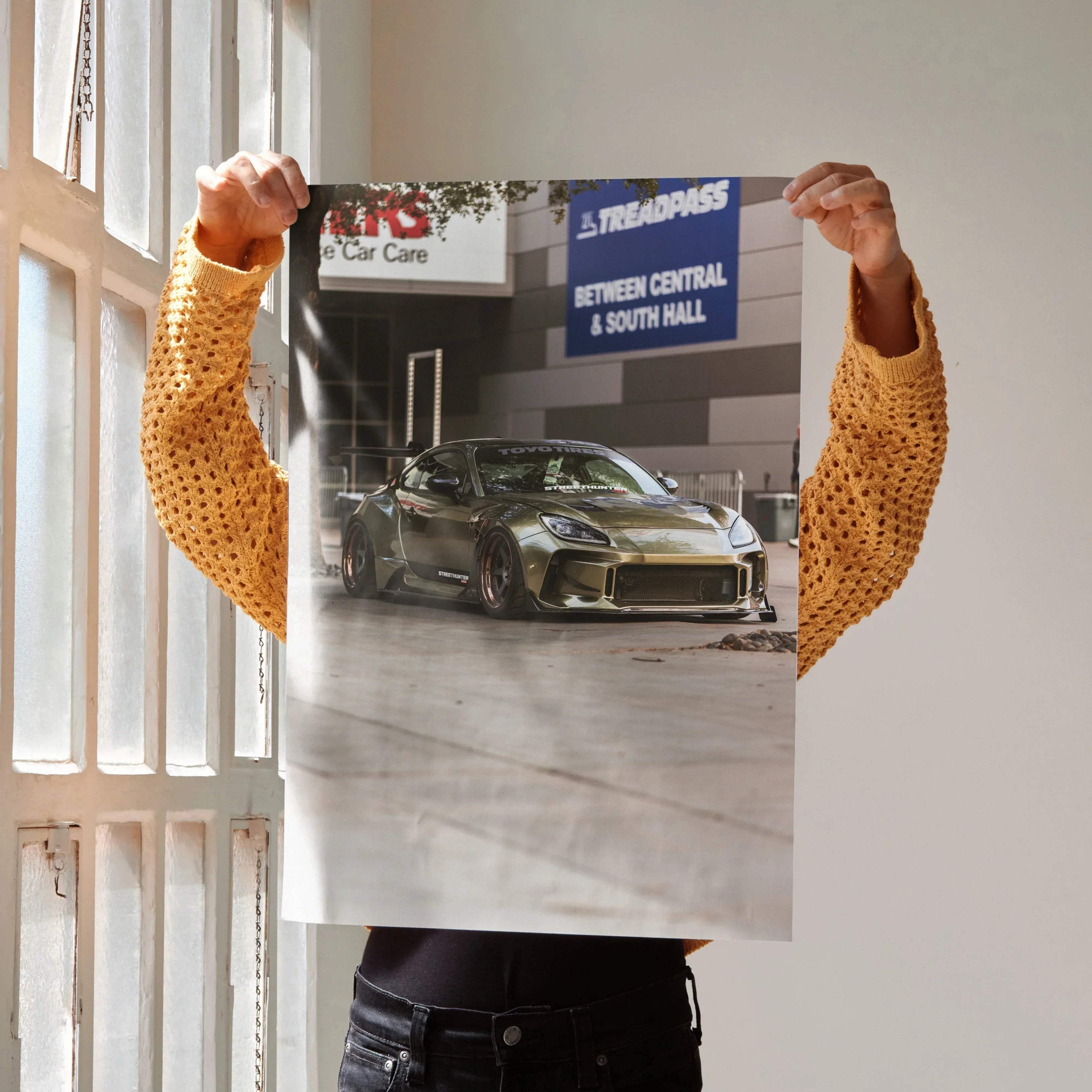 Subaru BRZ sports car poster with metallic green finish, satin wall art decor held by person in mustard sweater.
