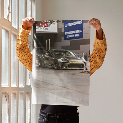 Subaru BRZ sports car poster with metallic green finish, satin wall art decor held by person in mustard sweater.