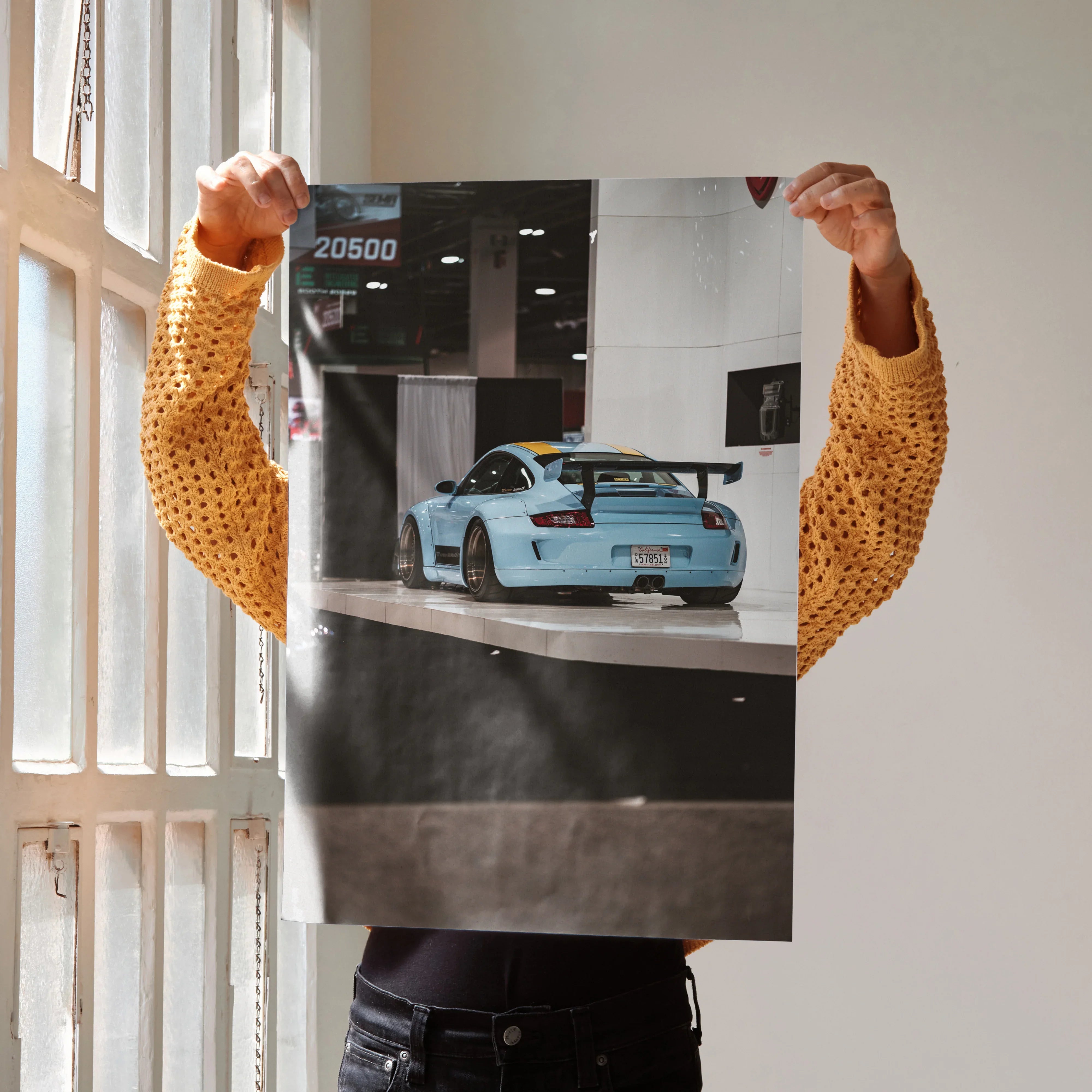 Porsche 911 Carrera 4 blue sports car poster held as wall art in bright room.