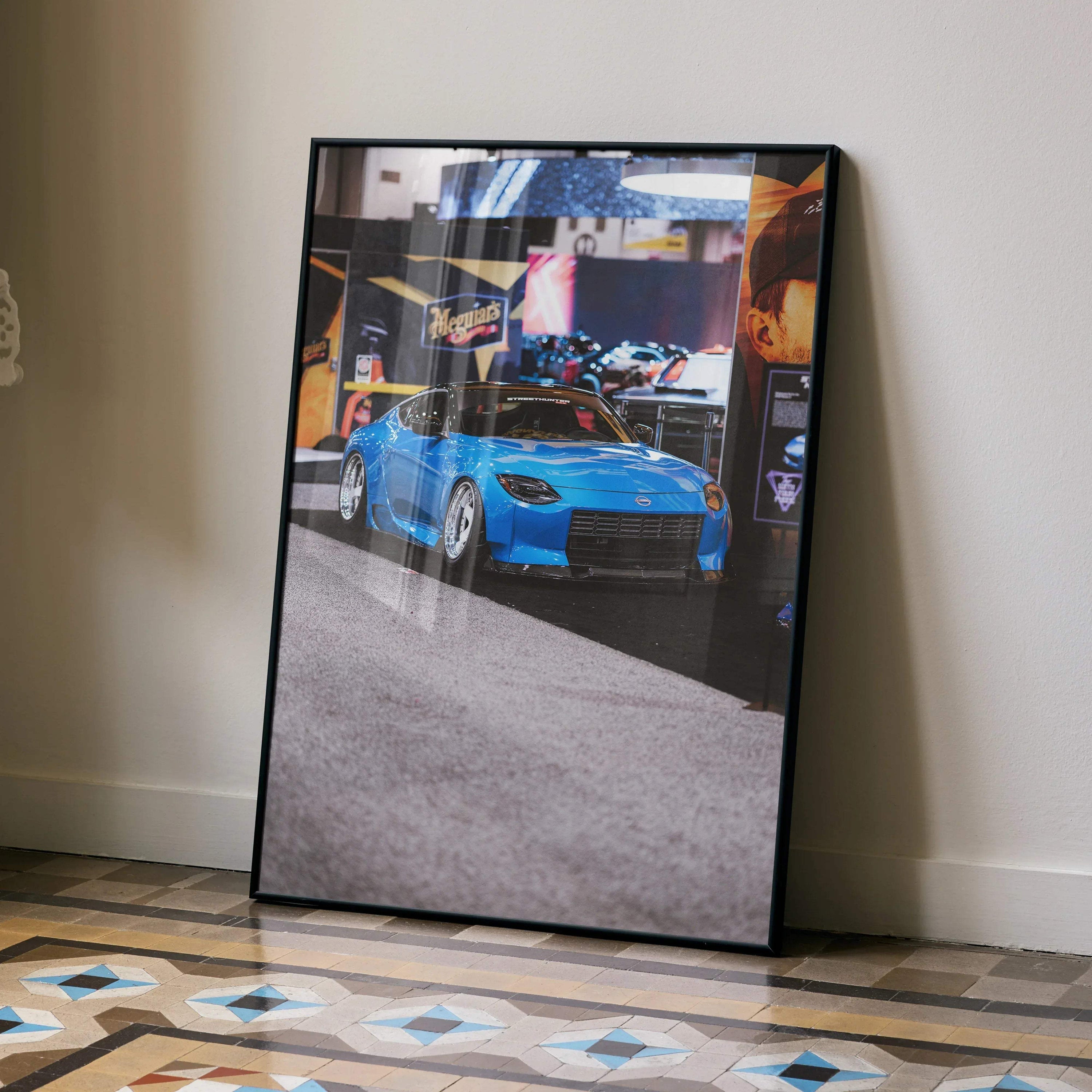 Nissan Z (RZ34) blue sports car poster framed wall art leaning against beige wall on patterned floor.