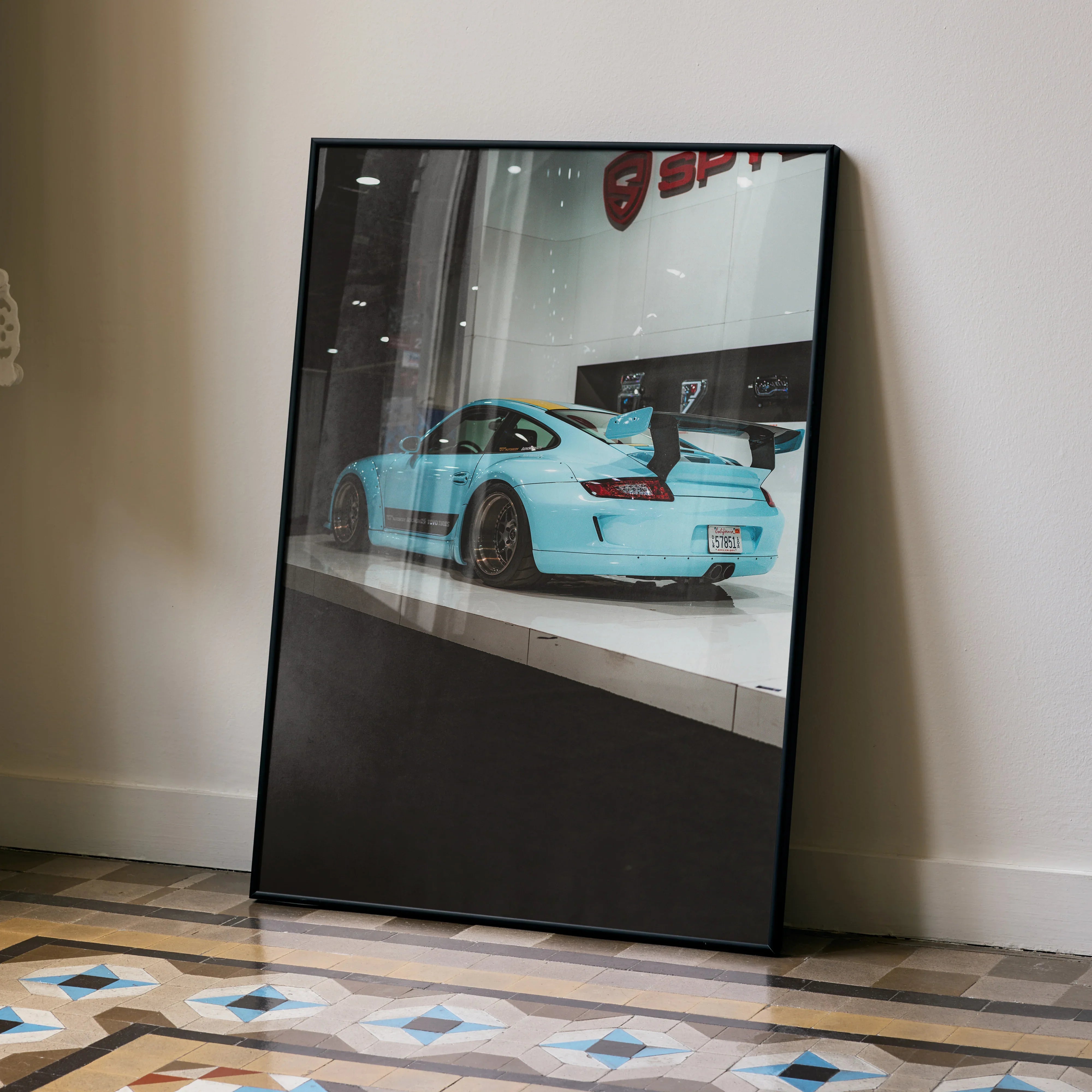 Porsche 911 Carrera 4 in light blue displayed on glossy poster leaning against beige wall, modern wall art decor.