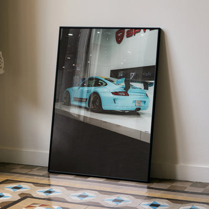 Porsche 911 Carrera 4 in light blue displayed on glossy poster leaning against beige wall, modern wall art decor.