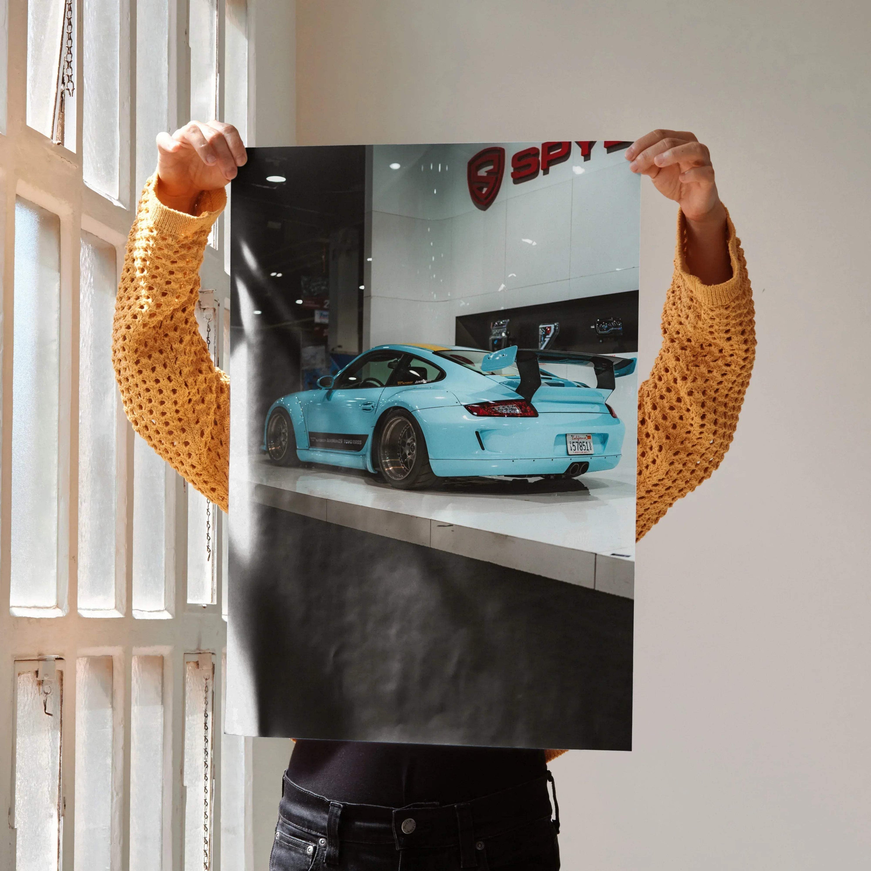 Porsche 911 Carrera 4 blue sports car poster held against light wall, high-resolution wall art.