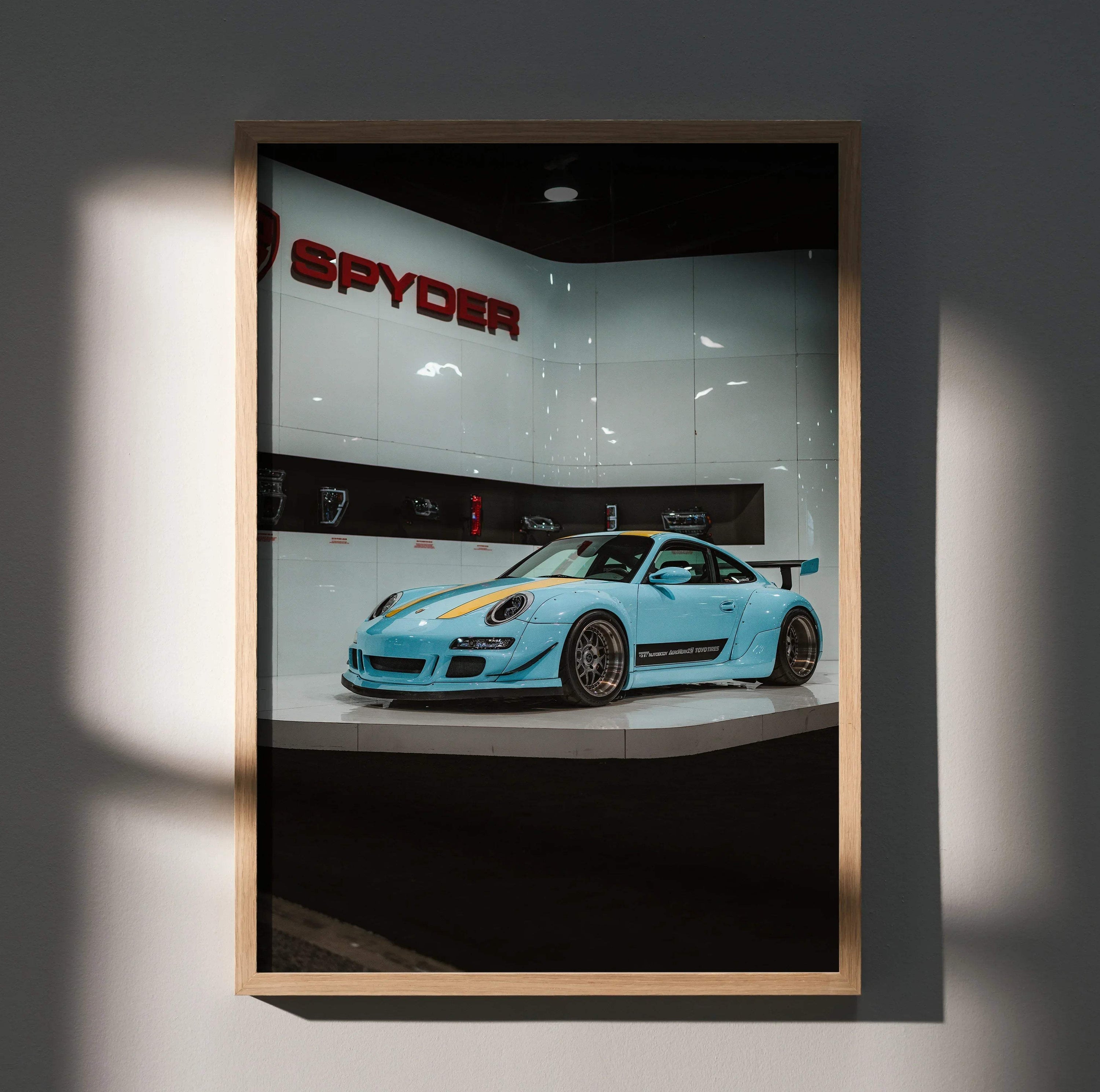 Porsche 911 Carrera 4 blue sports car poster wall art in wooden frame with Spyder sign backdrop.
