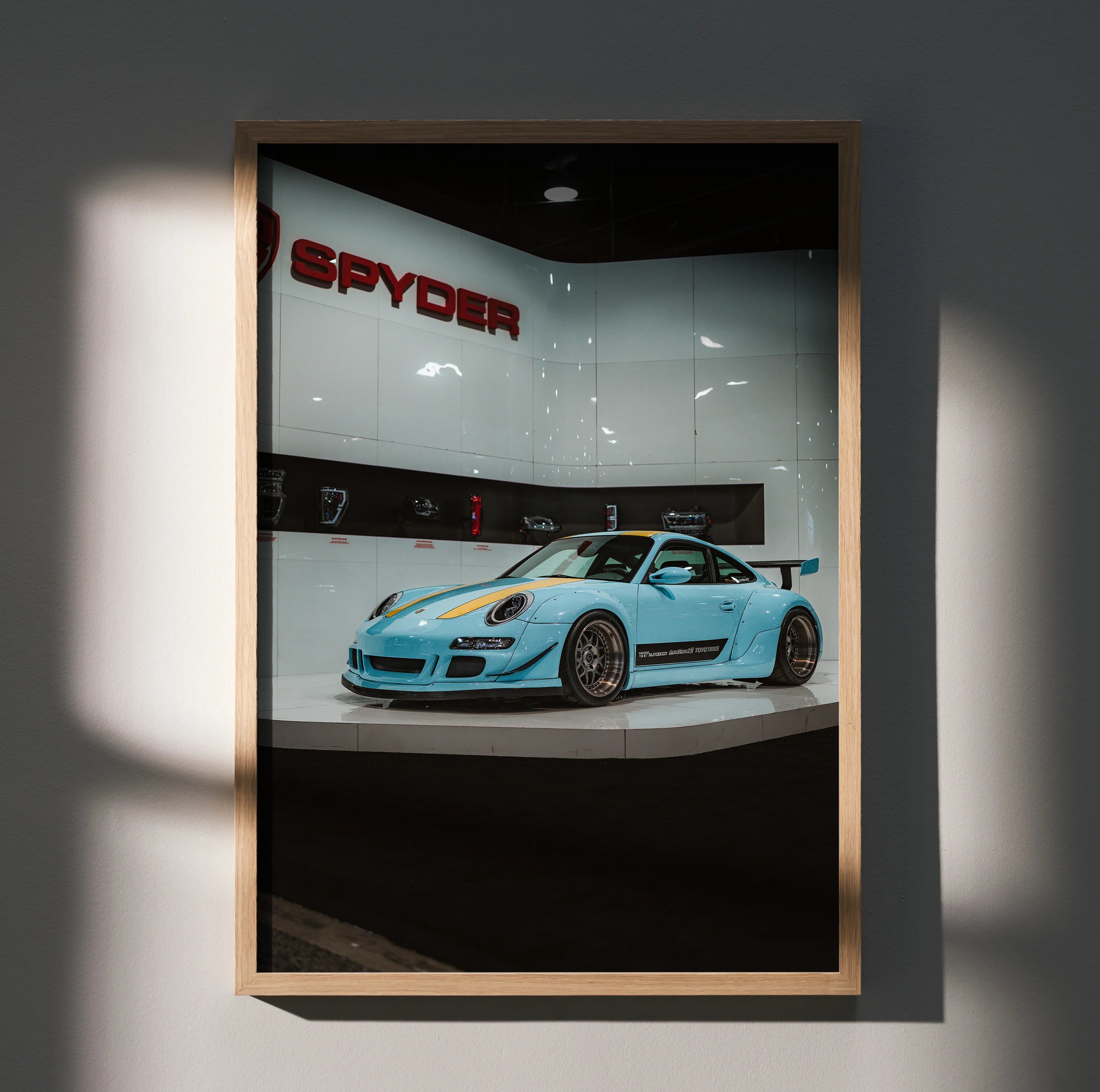 Porsche 911 Carrera 4 blue sports car poster wall art in wooden frame with Spyder sign backdrop.