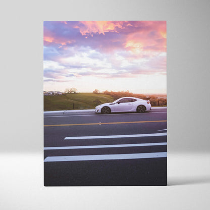 White Toyota FRS car on road at sunset with pink and orange sky canvas wall art.