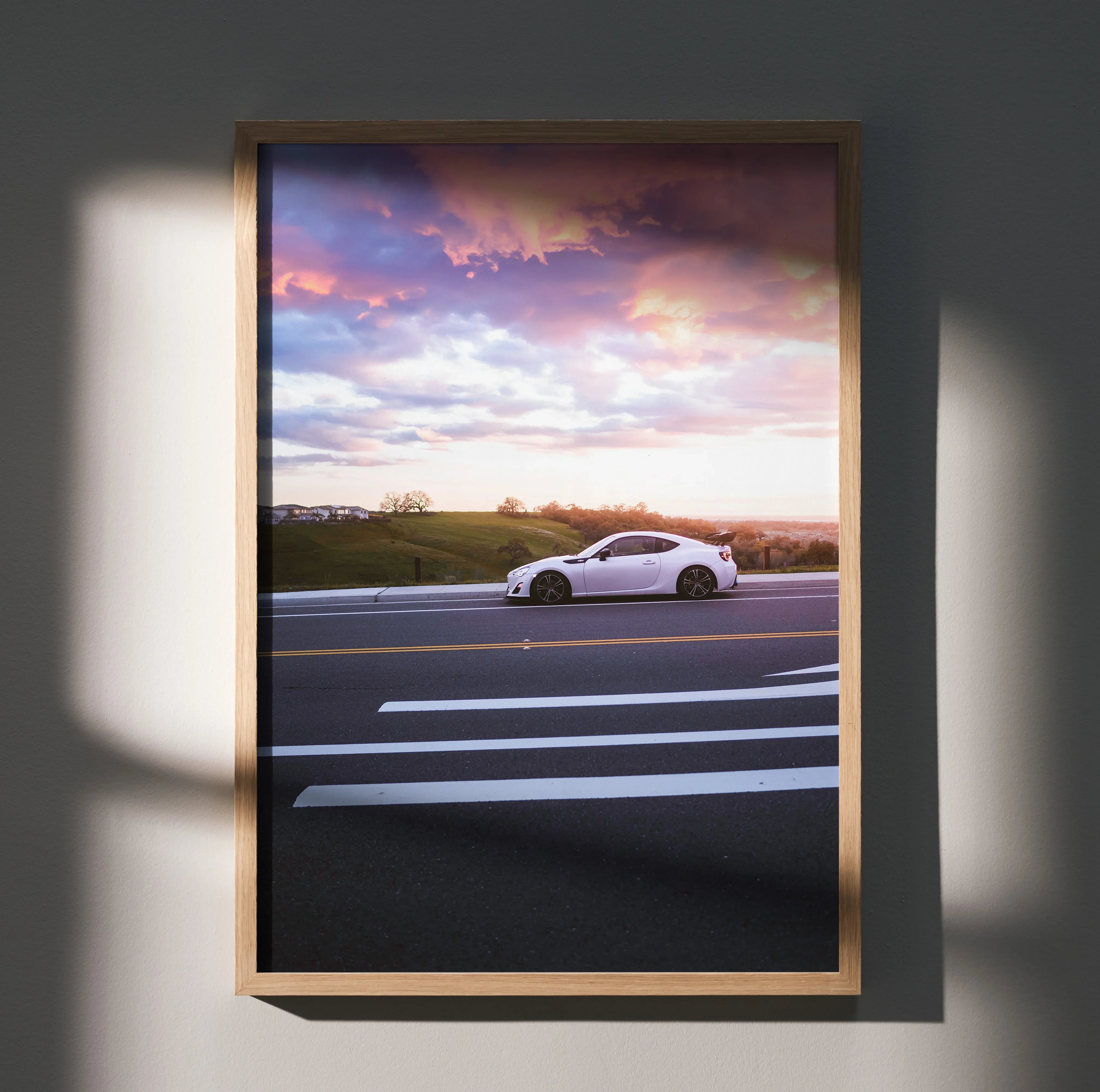 Toyota FRS driving on highway at sunset poster wall art with vibrant pink sky in wooden frame.