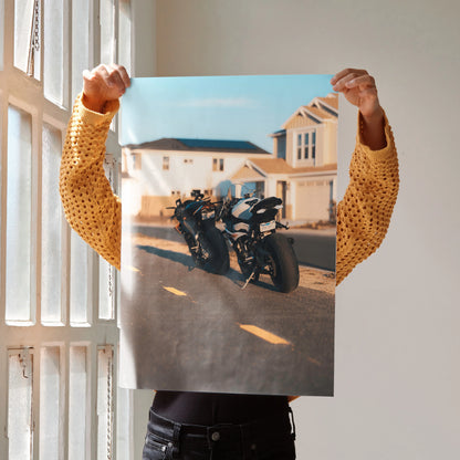 Poster wall art featuring BMW S1000RR and Aprilia RSV4 1100 motorcycles parked on a sunlit suburban street.