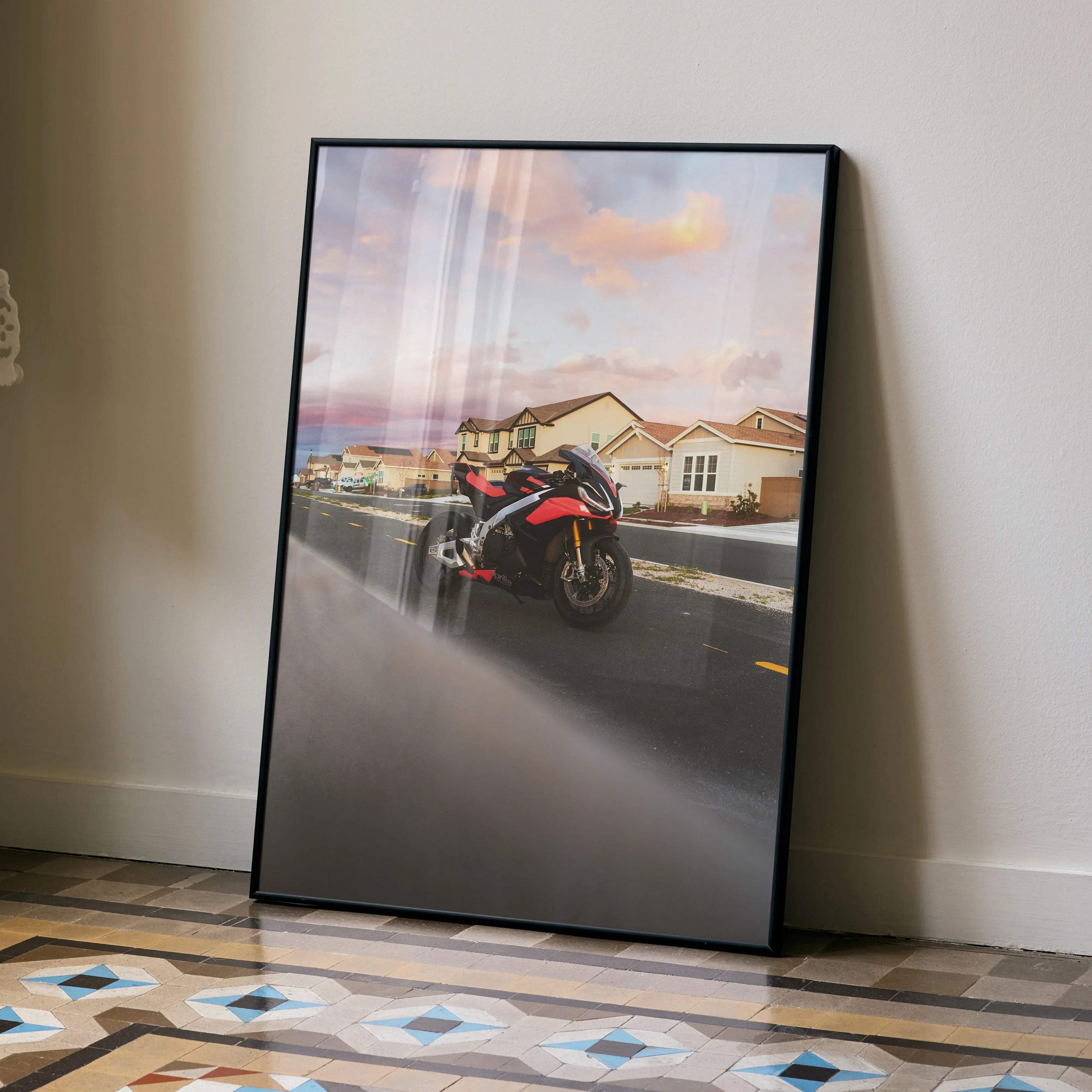 Black-framed aprilia rsv4 1100 factory motorcycle art print featuring a red and black bike on a suburban street under a pastel sky