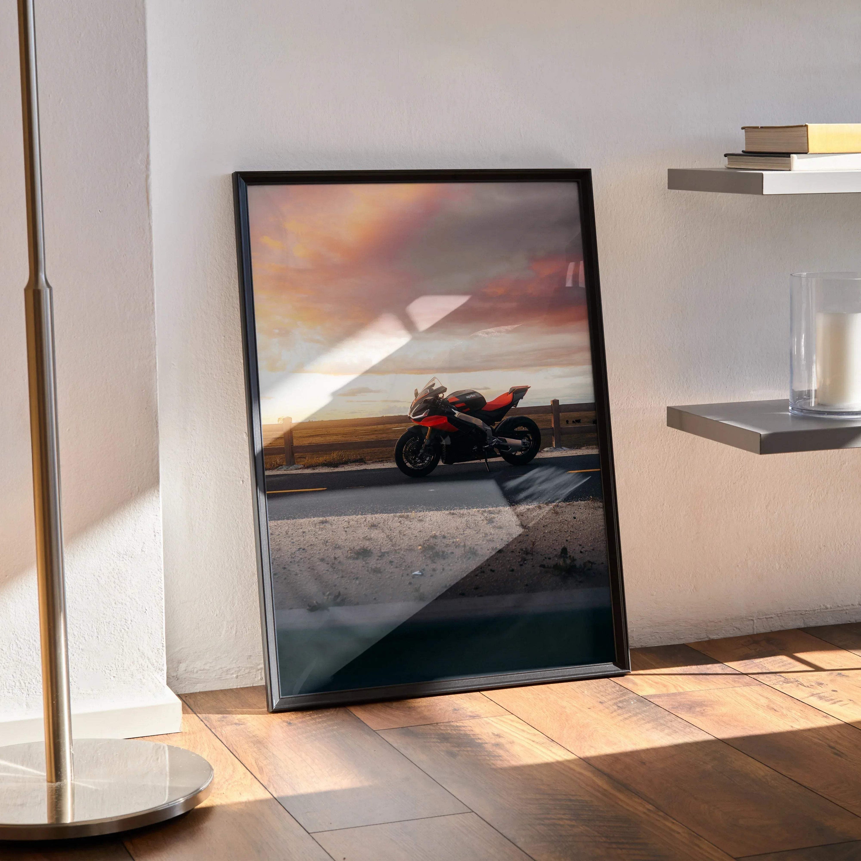 Aprilia RSV4 1100 Factory motorcycle poster with sunset sky, black frame wall art leaning on floor.