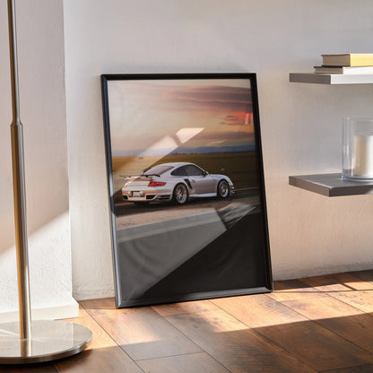 Porsche 911 Turbo poster with sunset backdrop framed wall art leaning against white wall on wooden floor.