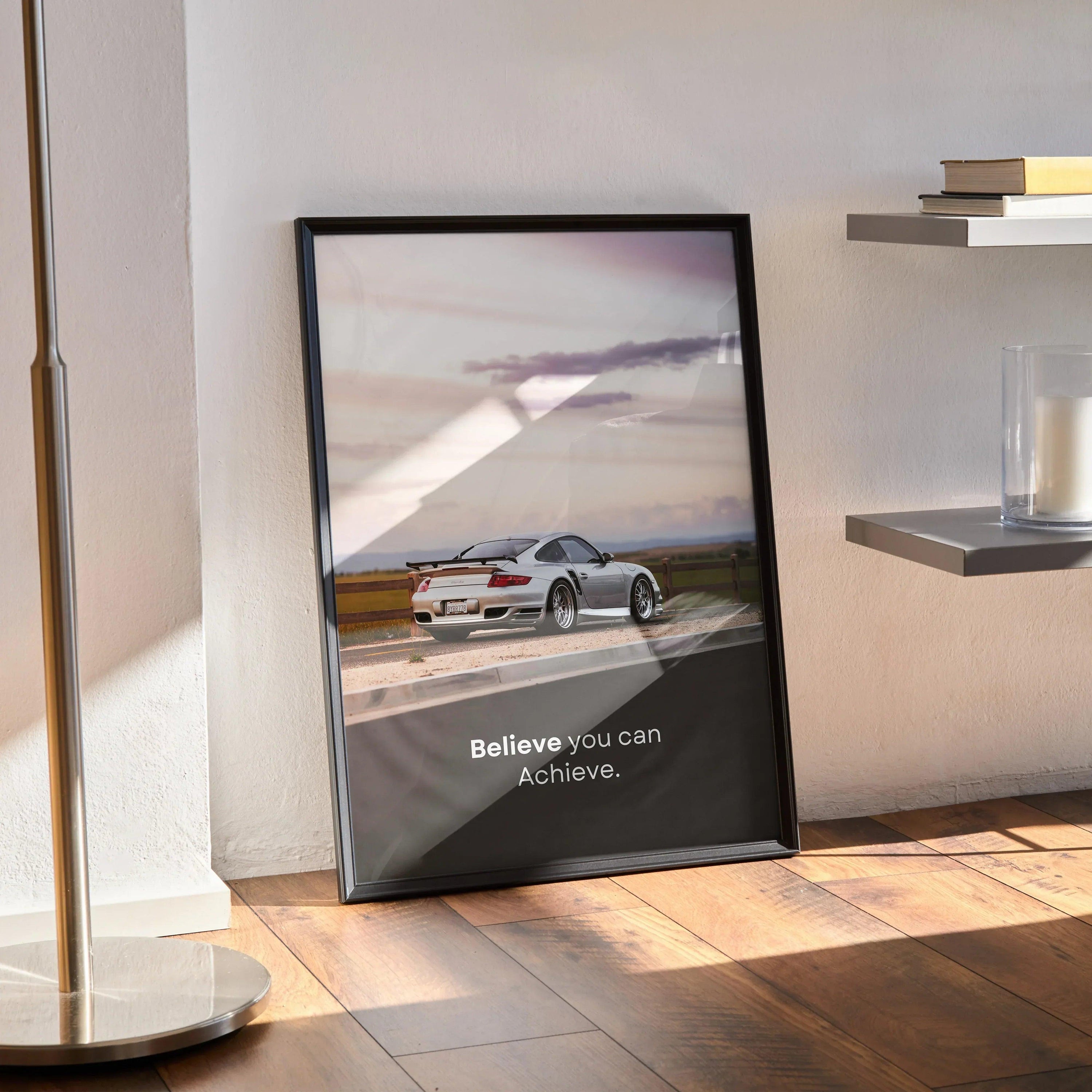 Porsche 911 Turbo wall art poster with inspiring text "Believe you can achieve" in black frame on wooden floor.