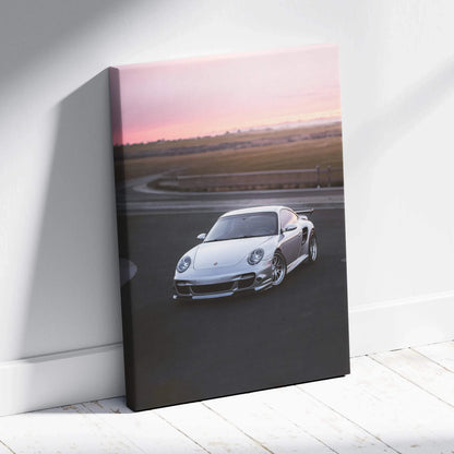 Vertical canvas wall art featuring a white Porsche 911 Turbo on a racetrack at sunset.