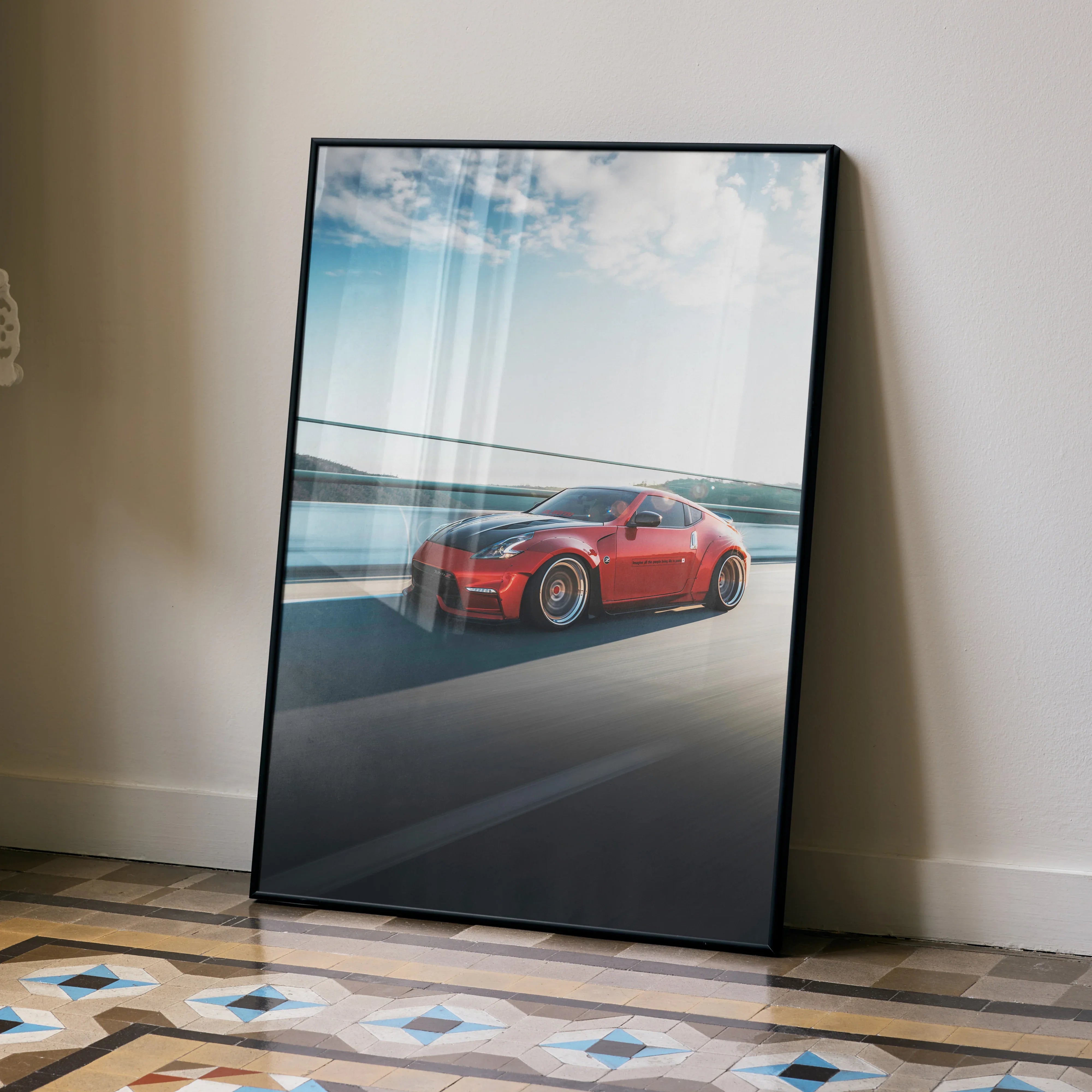 Red Nissan 370Z sports car on scenic coastline road poster leaning against wall, automotive wall art.