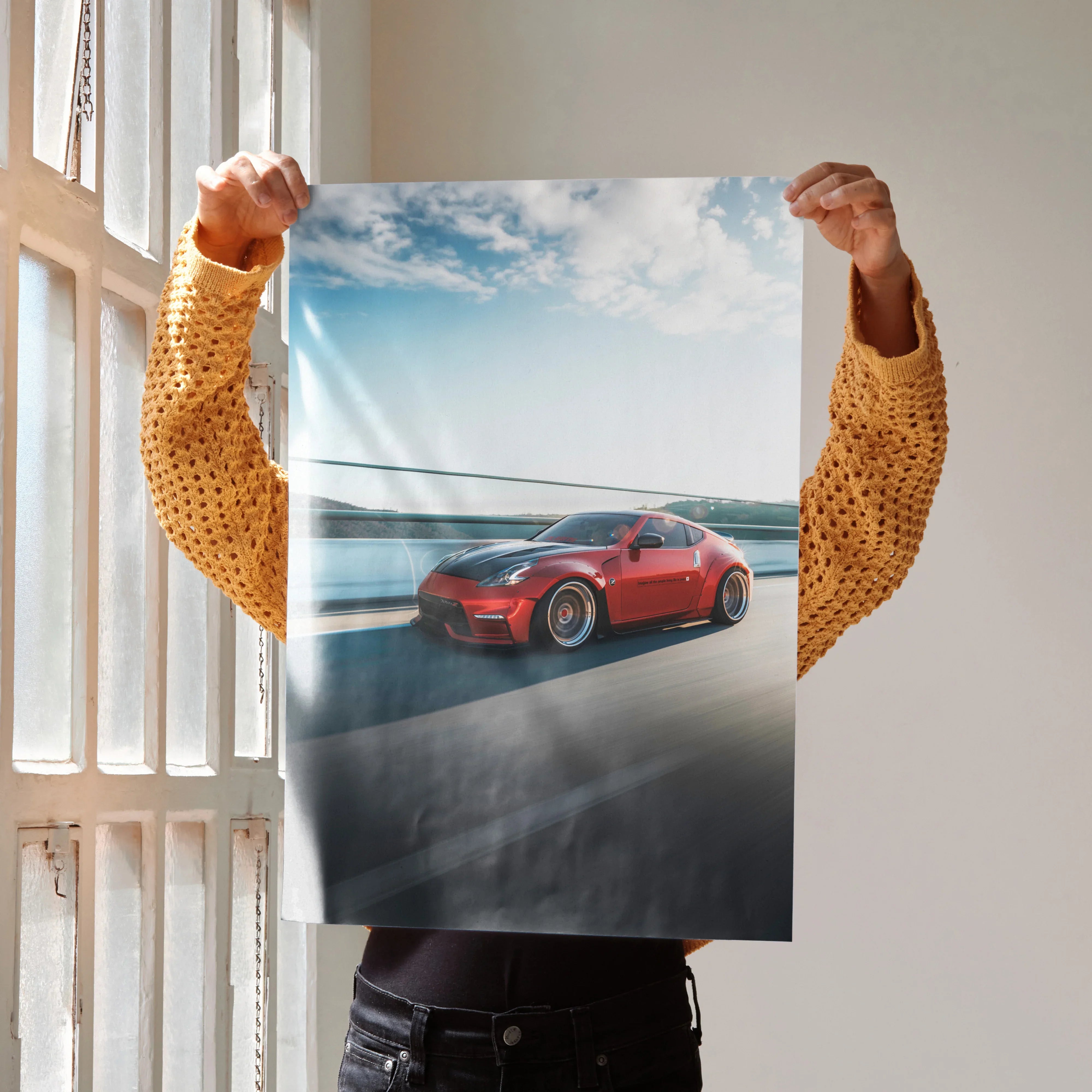 Red Nissan 370Z sports car driving on coastal road poster wall art with blue sky background.