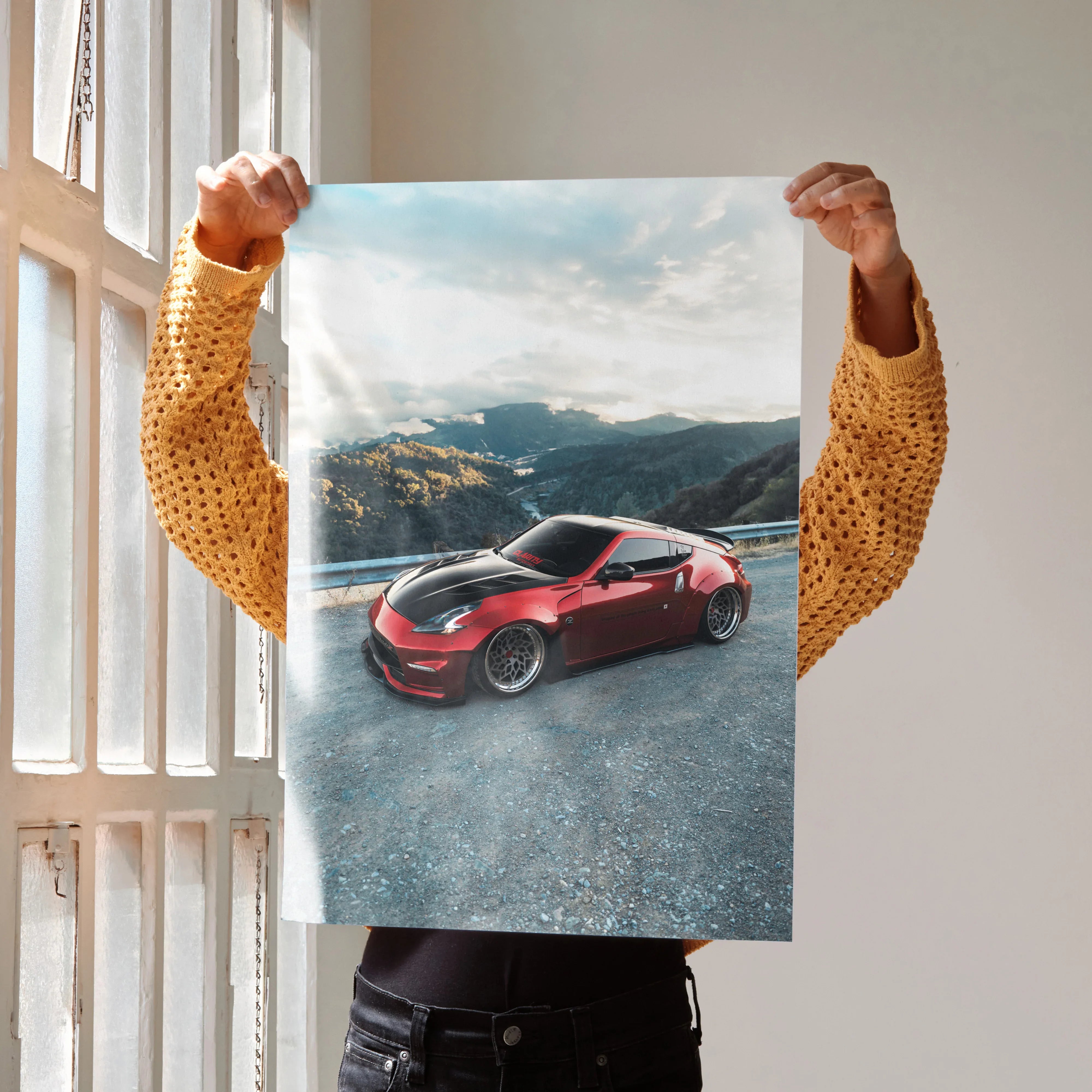 Red Nissan 370Z sports car on mountain road poster wall art with blue sky backdrop.