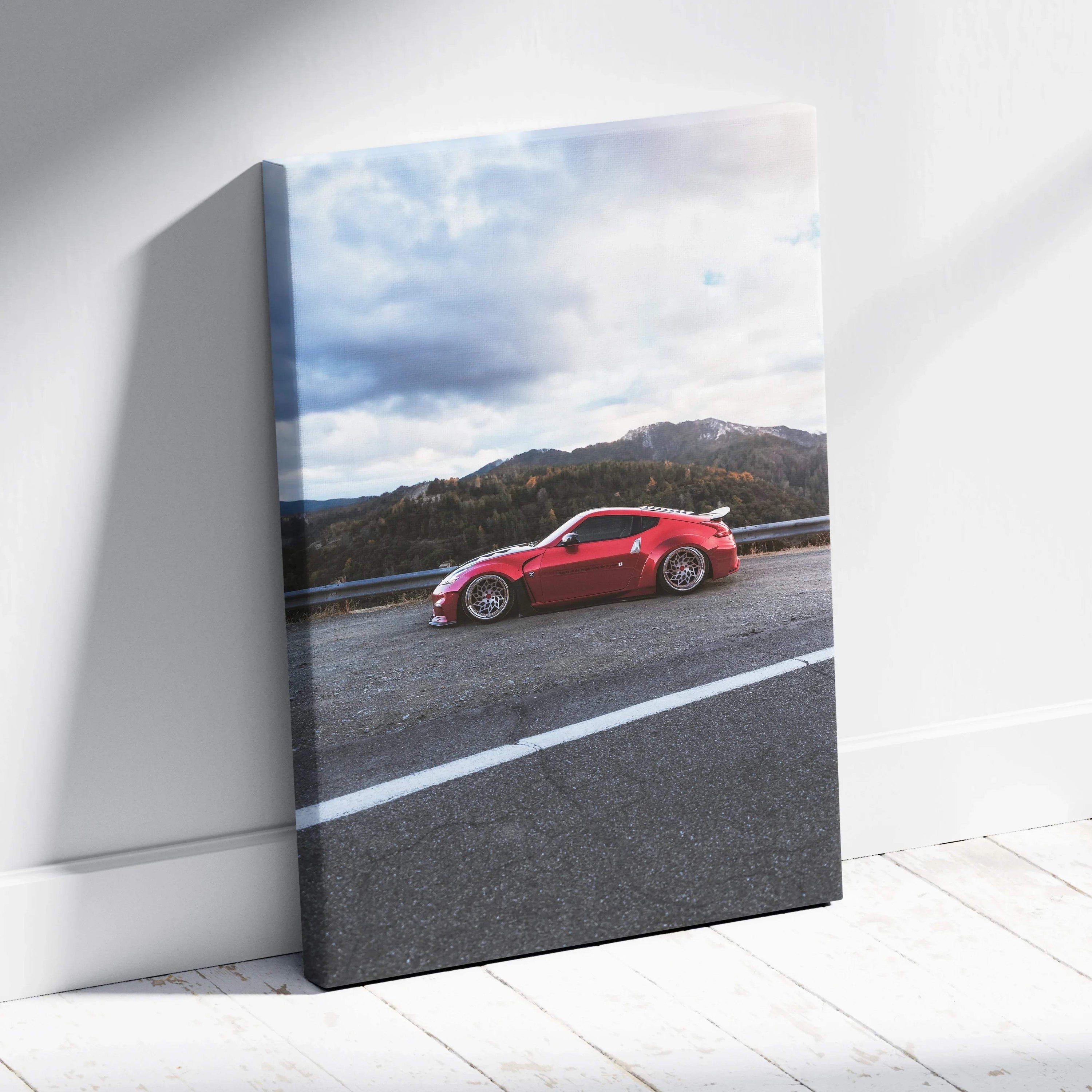 Red Nissan 370z on road with mountains and cloudy sky vertical canvas wall art.