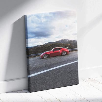 Red Nissan 370z on road with mountains and cloudy sky vertical canvas wall art.