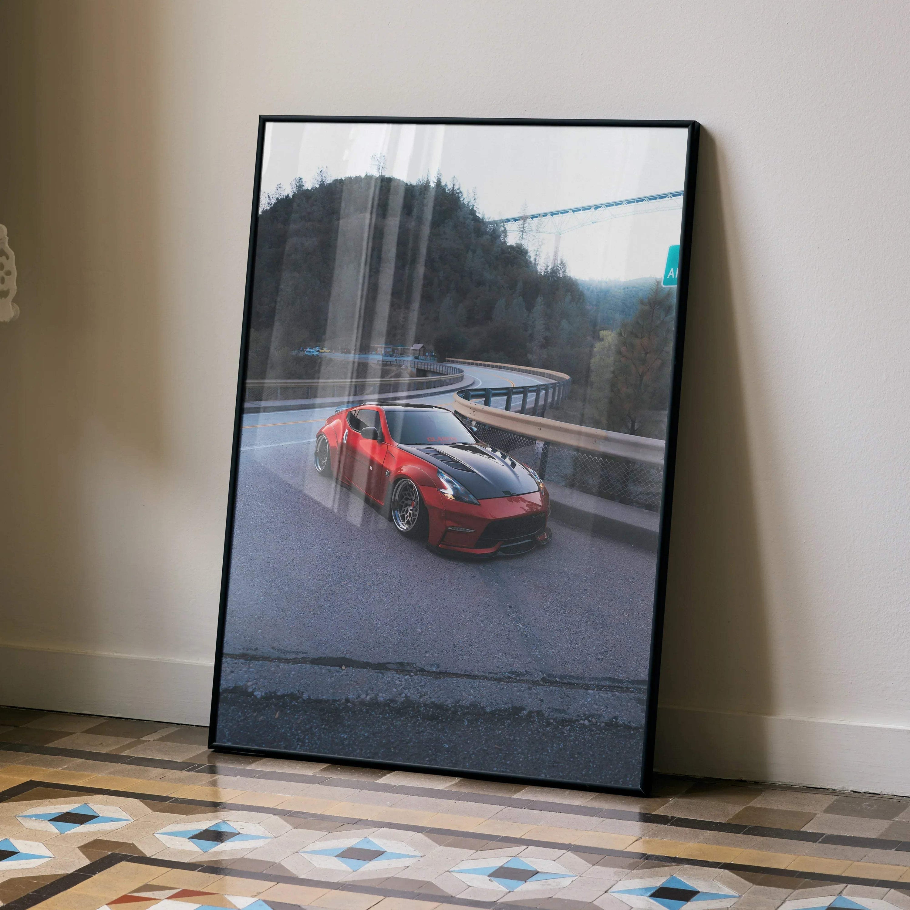 Red Nissan 370z driving on winding road poster, framed wall art with scenic mountain background.