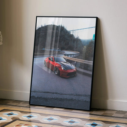 Red Nissan 370z driving on winding road poster, framed wall art with scenic mountain background.