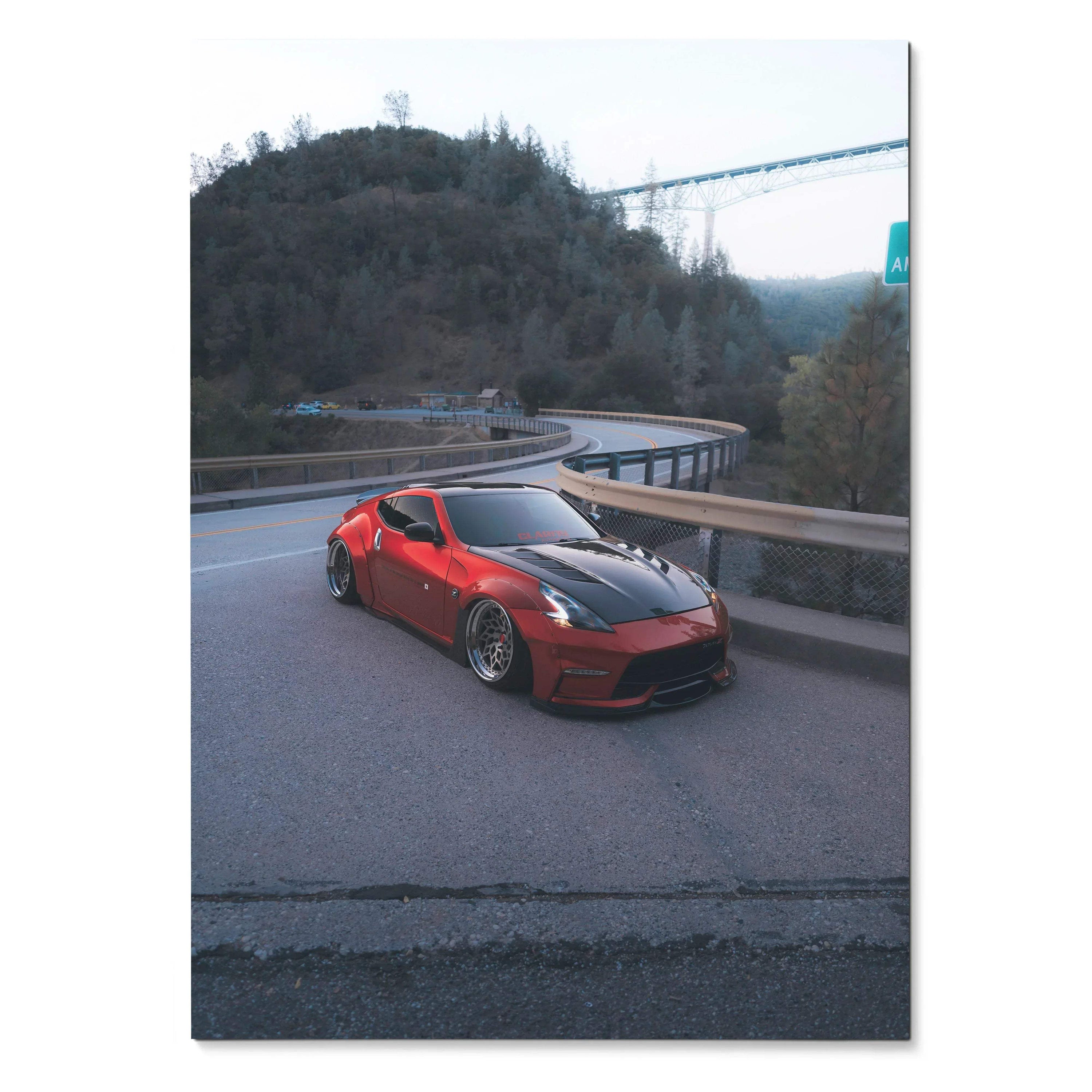 Red Nissan 370z on curving mountain road poster wall art with bridge and trees background.