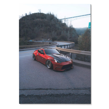 Red Nissan 370z on curving mountain road poster wall art with bridge and trees background.
