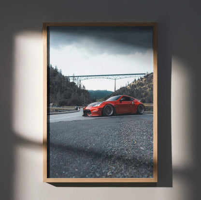 Nissan 370Z red sports car on gravel with mountain bridge background poster wall art.
