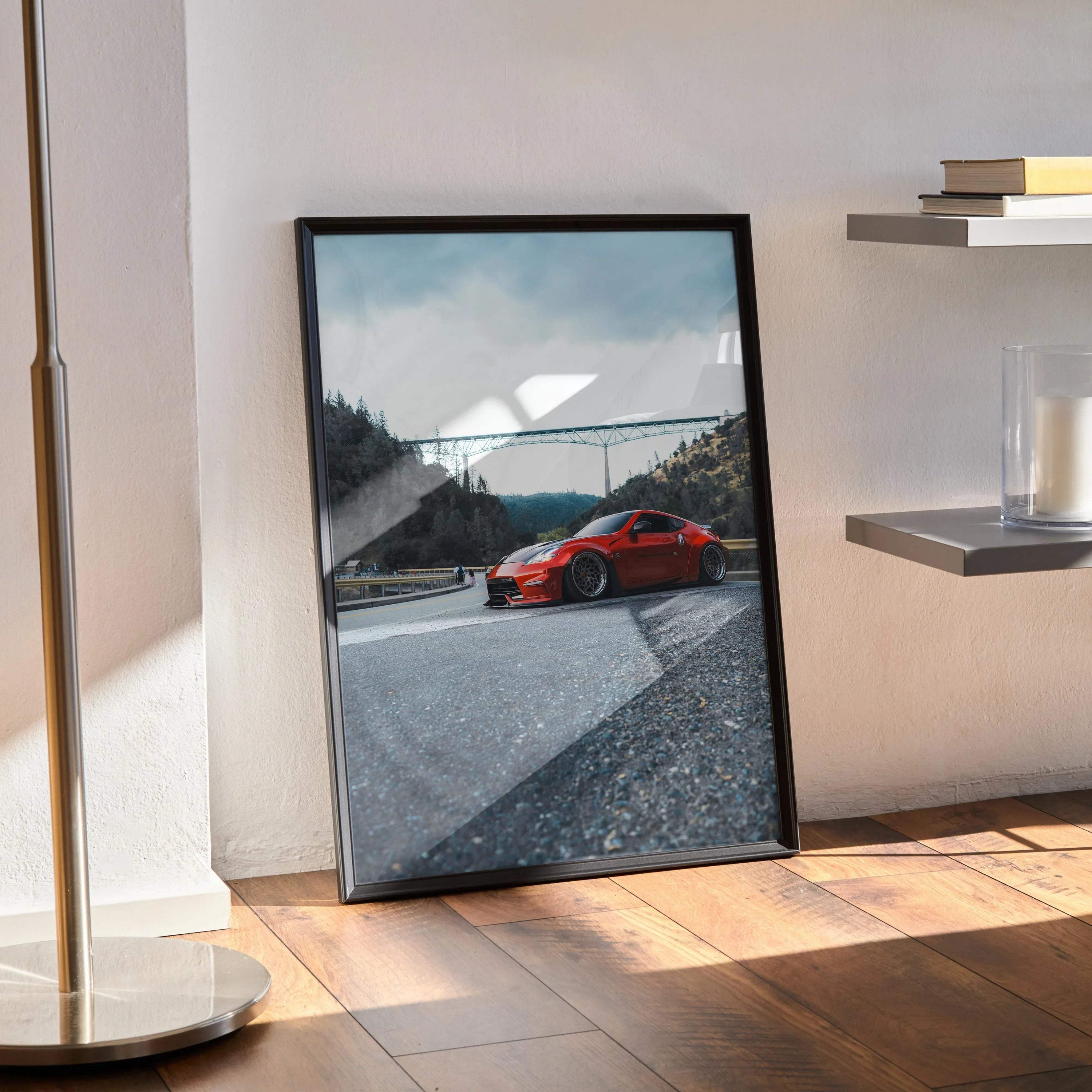 Nissan 370Z red sports car poster framed on floor with mountain road wall art background.