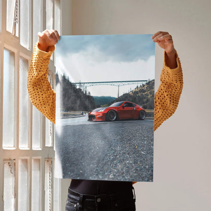 Red Nissan 370Z poster on textured road with bridge and cloudy sky background wall art.