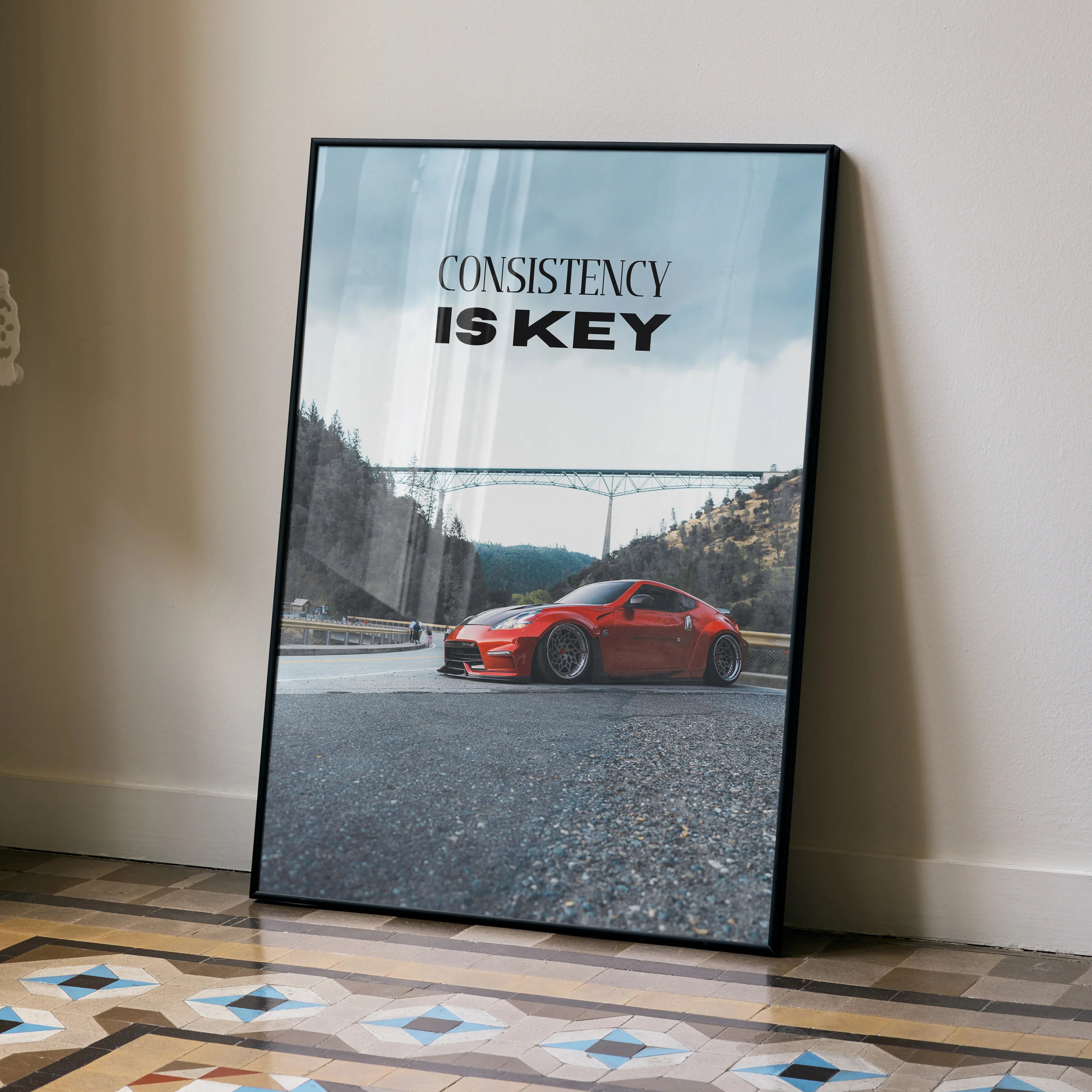 Motivational poster wall art featuring a red Nissan 370z with "Consistency is Key" text against a sky background.