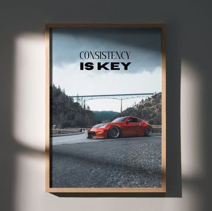 Motivational wall art poster with red Nissan 370z and text "Consistency Is Key" against mountain and bridge background.