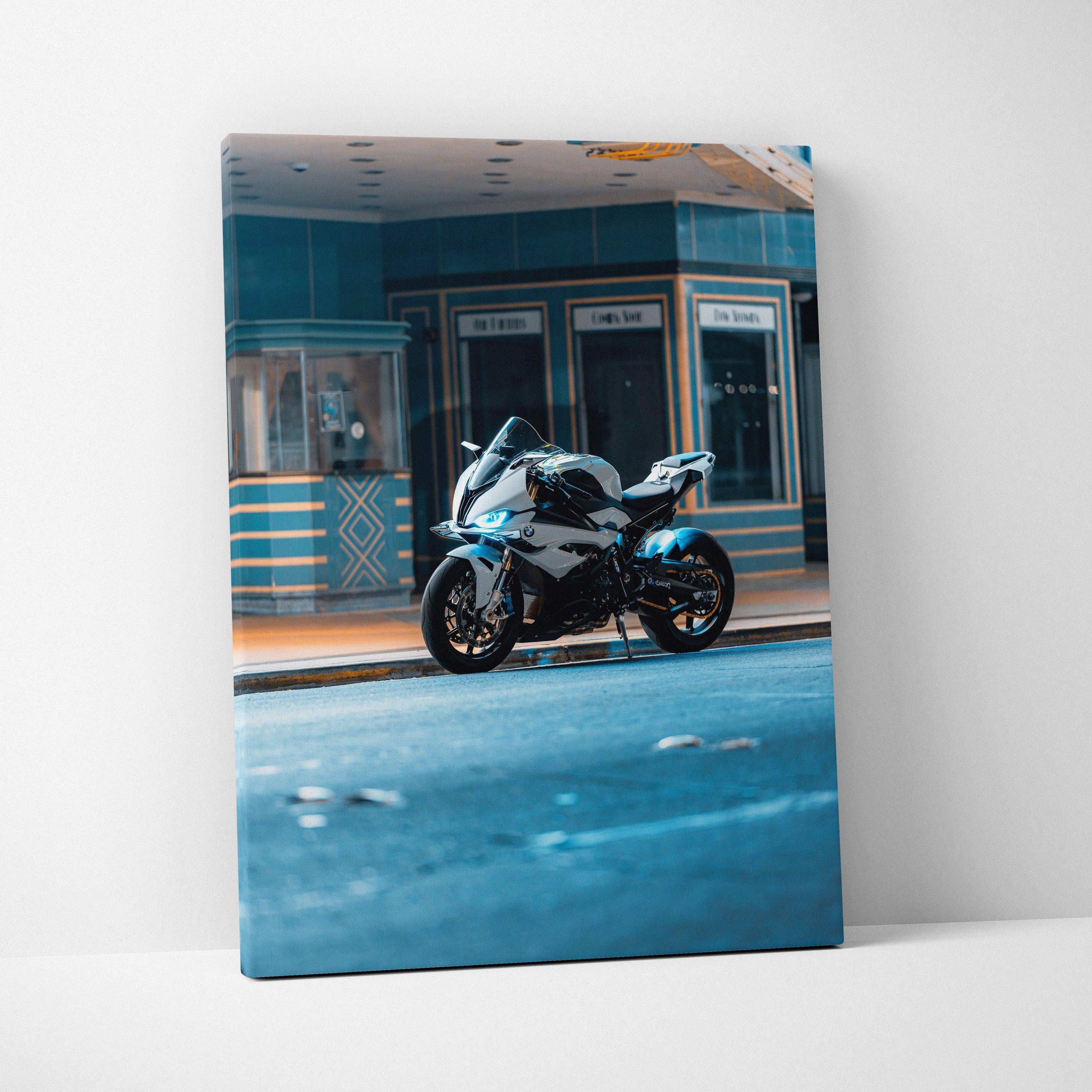 Vertical canvas wall art featuring a sleek black BMW S1000RR motorcycle against a vintage blue and yellow building backdrop.