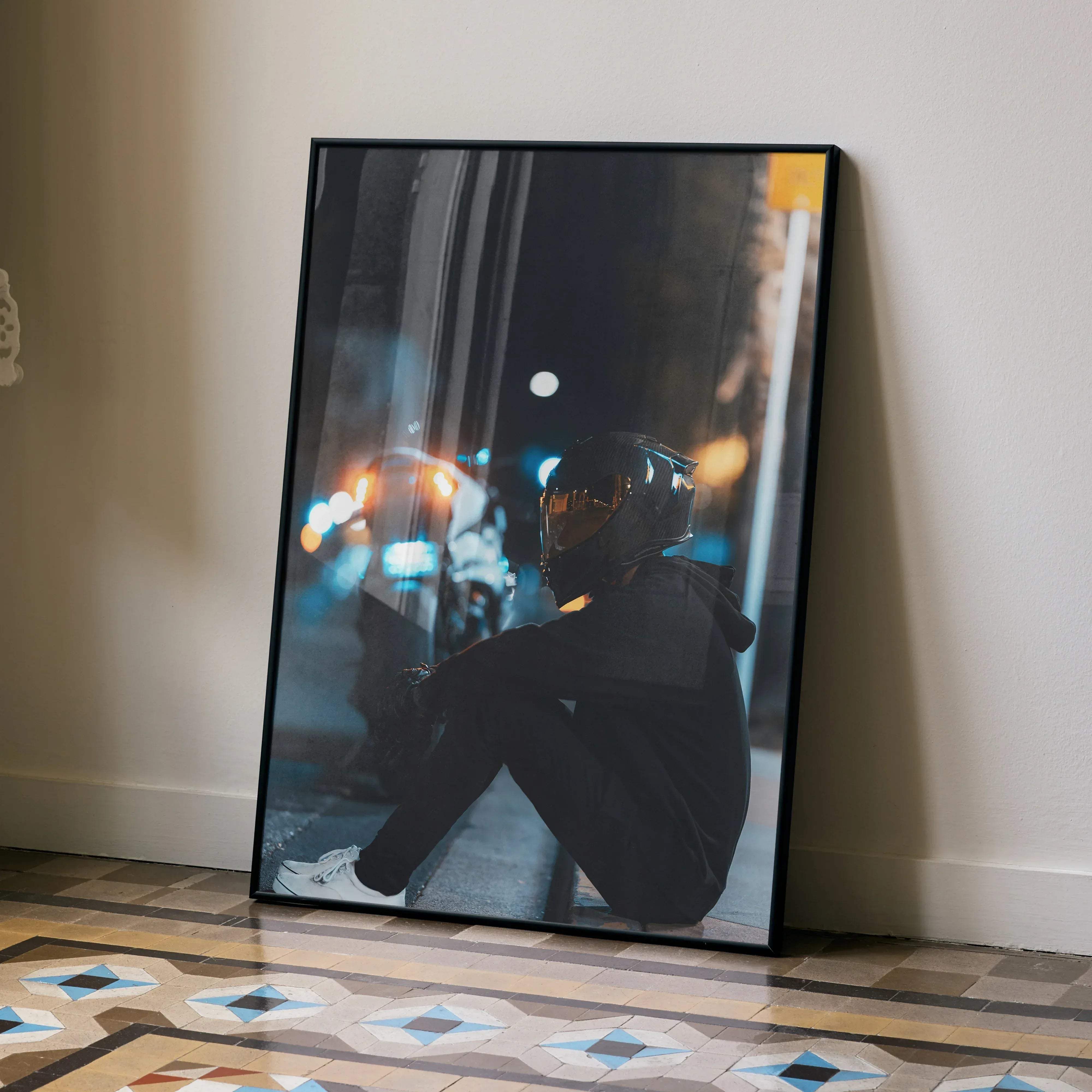 Black-framed art print of a male biker with a reflective gold scorpion r1 helmet sitting on a city street at night