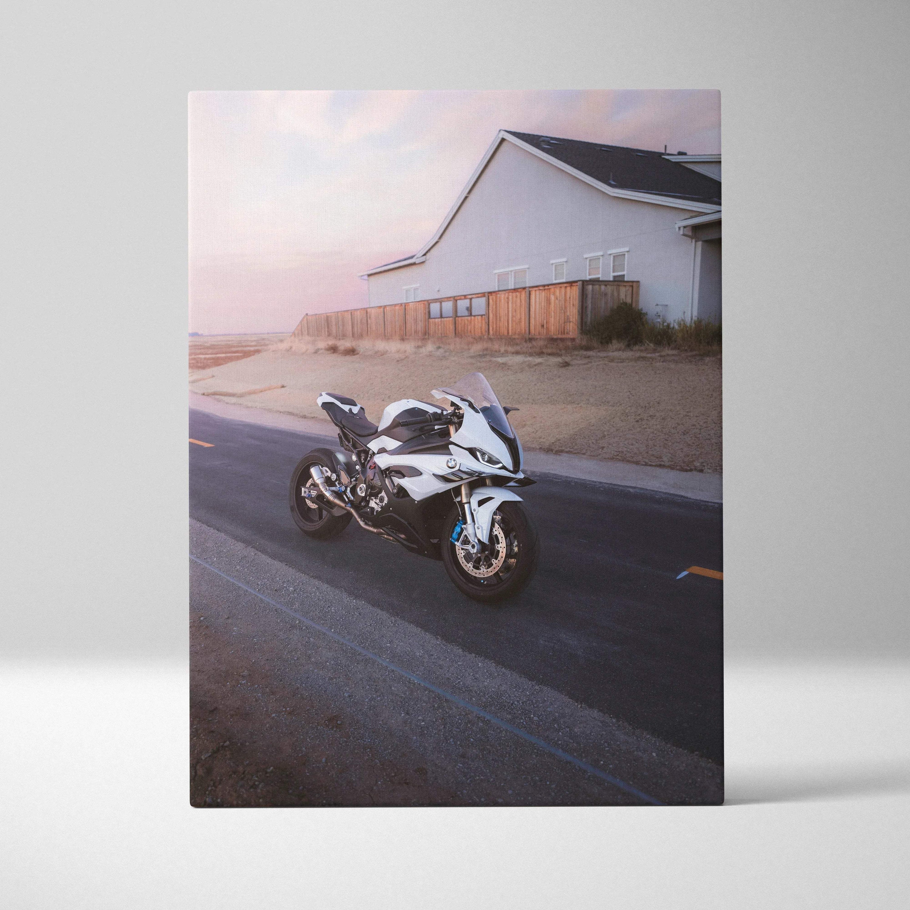 Vertical canvas art of a white BMW S1000RR motorcycle on a road near a coastal house at sunset.