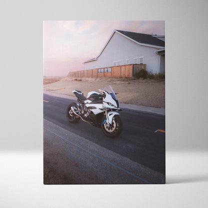 Vertical canvas art of a white BMW S1000RR motorcycle on a road near a coastal house at sunset.