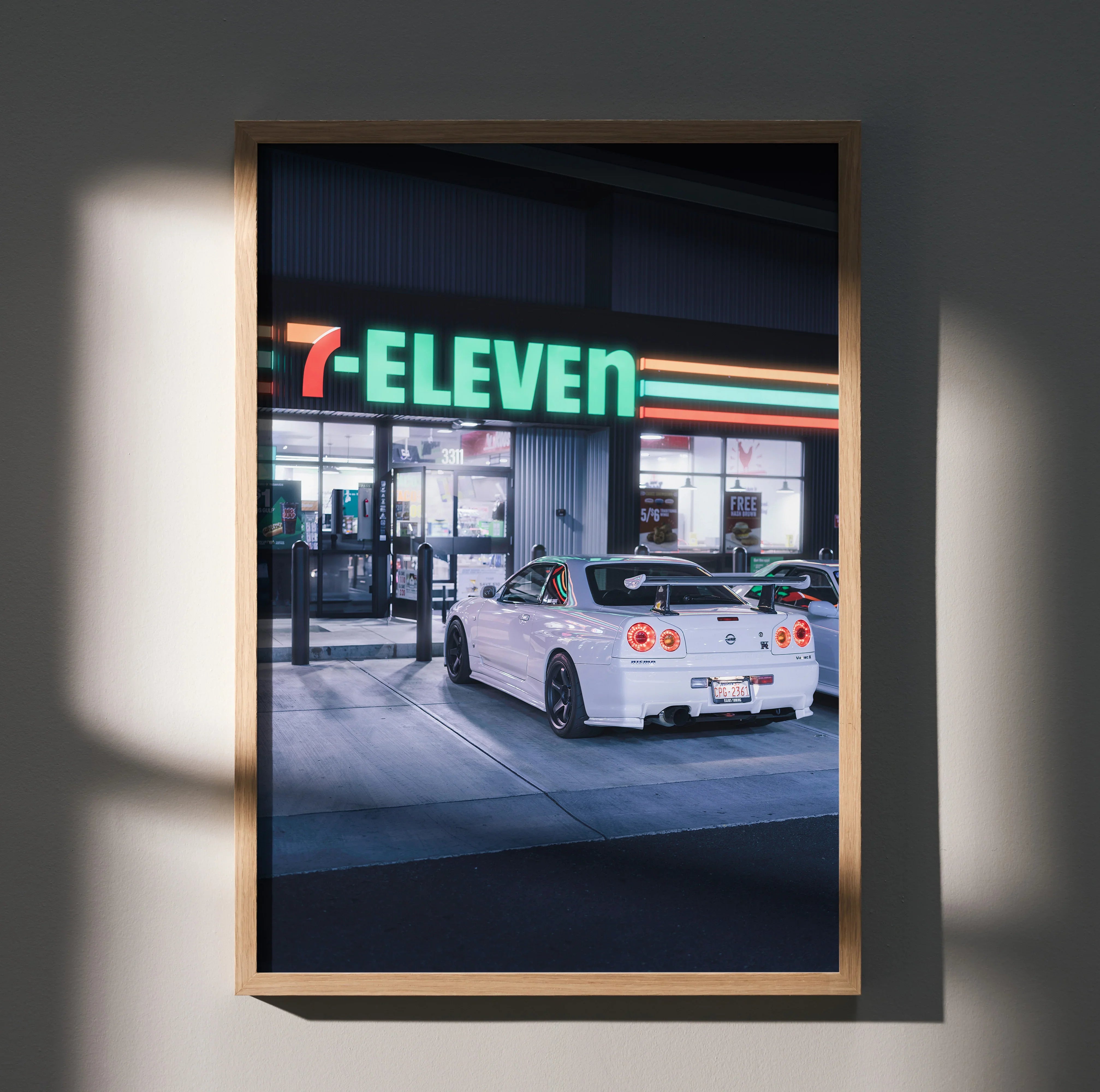 Nissan GTR R34 Skyline poster wall art showing white car parked at 7-Eleven gas station at night.