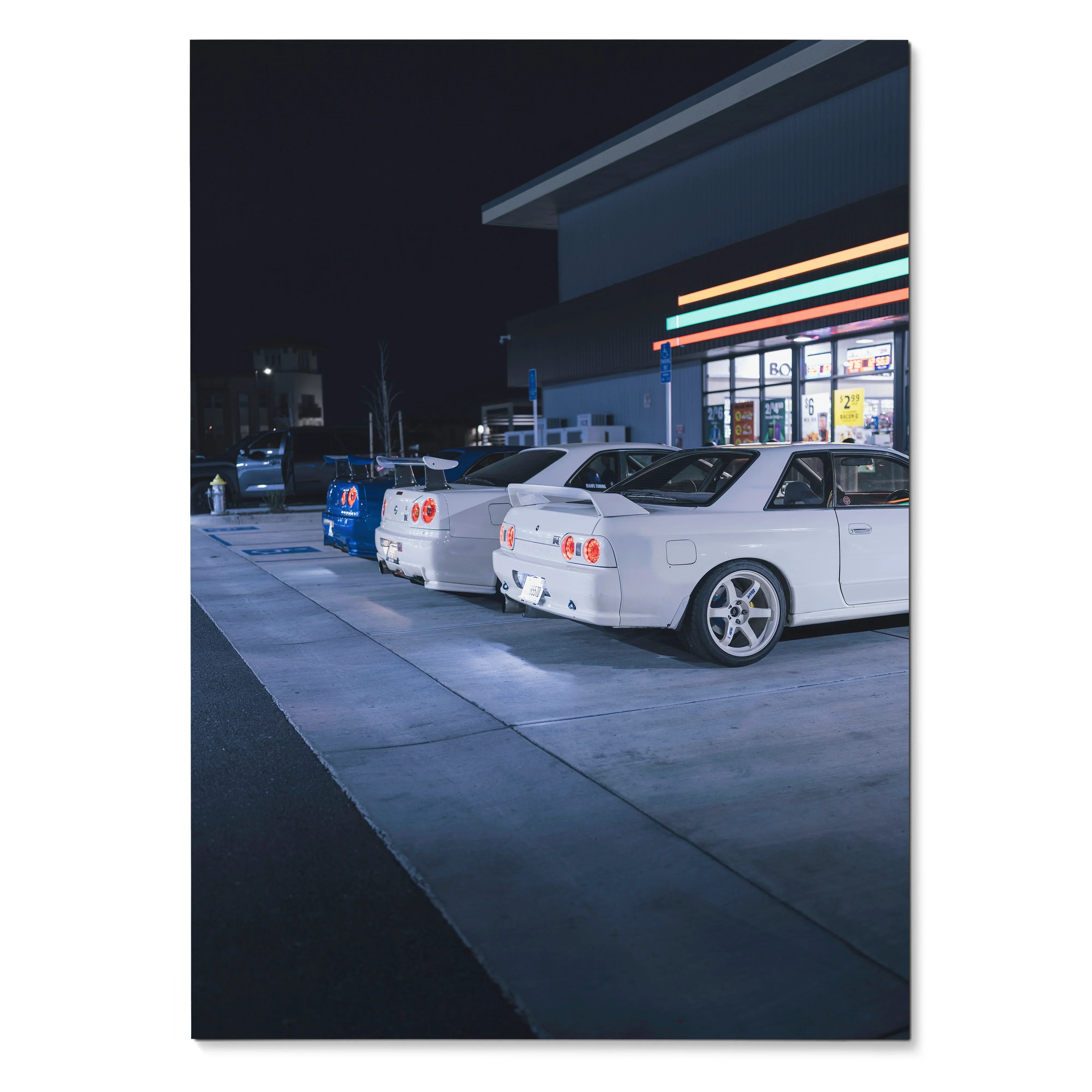 Poster of three Nissan GTR Skyline cars parked in front of a lit store at night wall art.