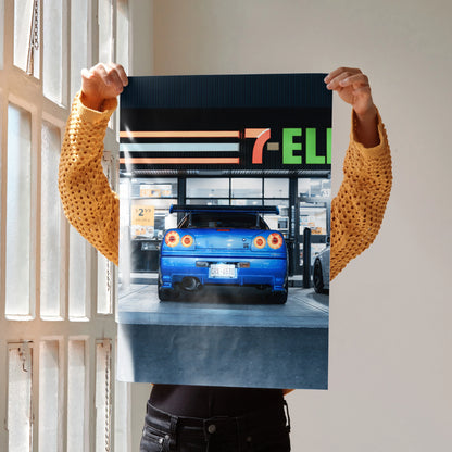 Blue Nissan GTR R34 Skyline poster held indoors, featuring gas station wall art with 7-Eleven signage.