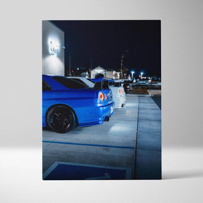 Vertical canvas art featuring blue and white Nissan GTR R34 Skylines parked at night, high-resolution wall art.