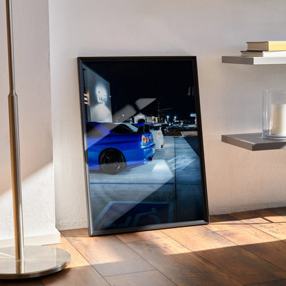 Nissan R34 GTR Skyline poster with blue sports car at night, framed wall art leaning on floor.