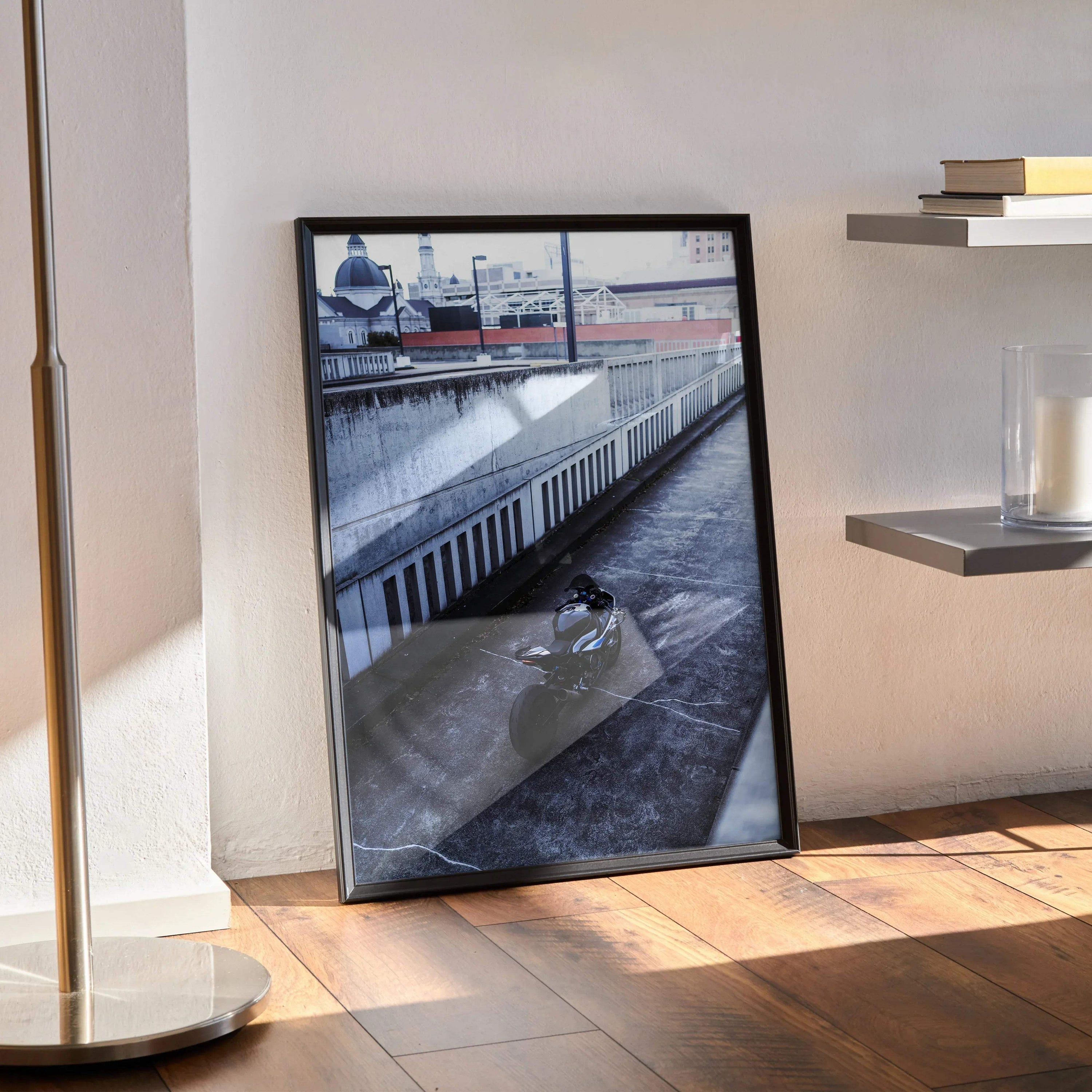 BMW S1000RR motorcycle poster leaning against wall, framed black wall art in bright room with hardwood floor.