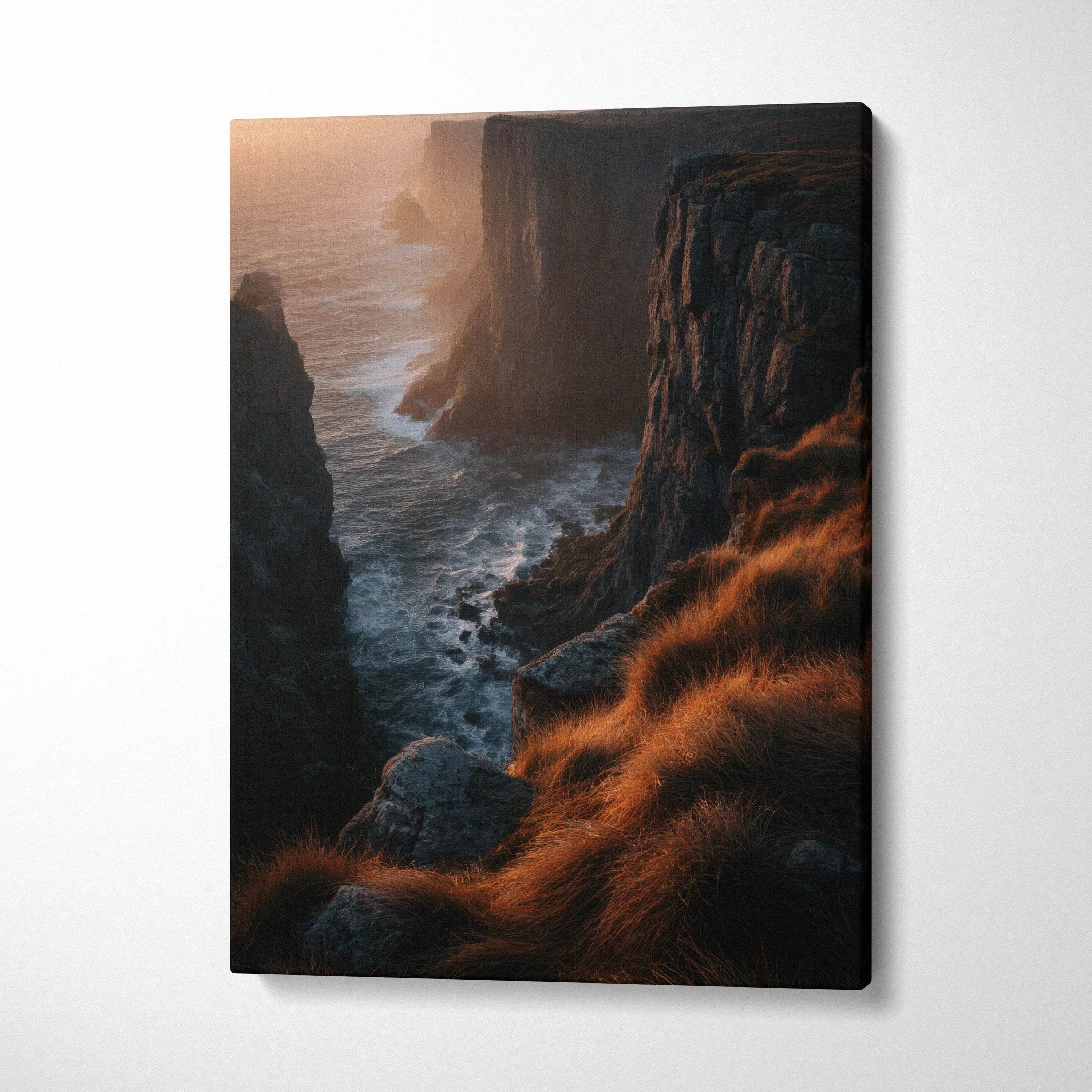 Vertical canvas wall art of a sunset-lit rocky cliff with golden grasses and ocean waves below.