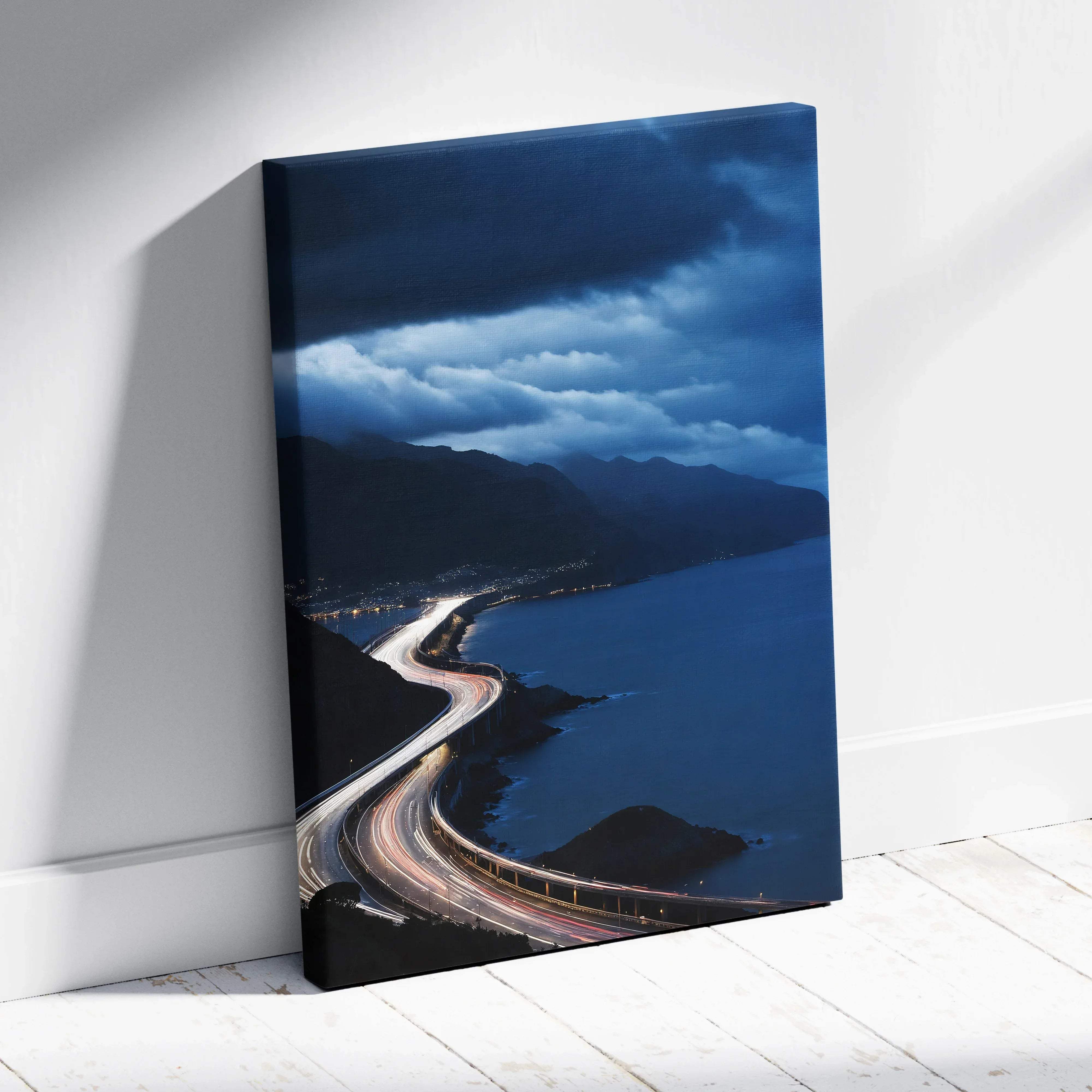 A sleek rectangular canvas print of a moody blue coastal highway at night with glowing light trails and mountains