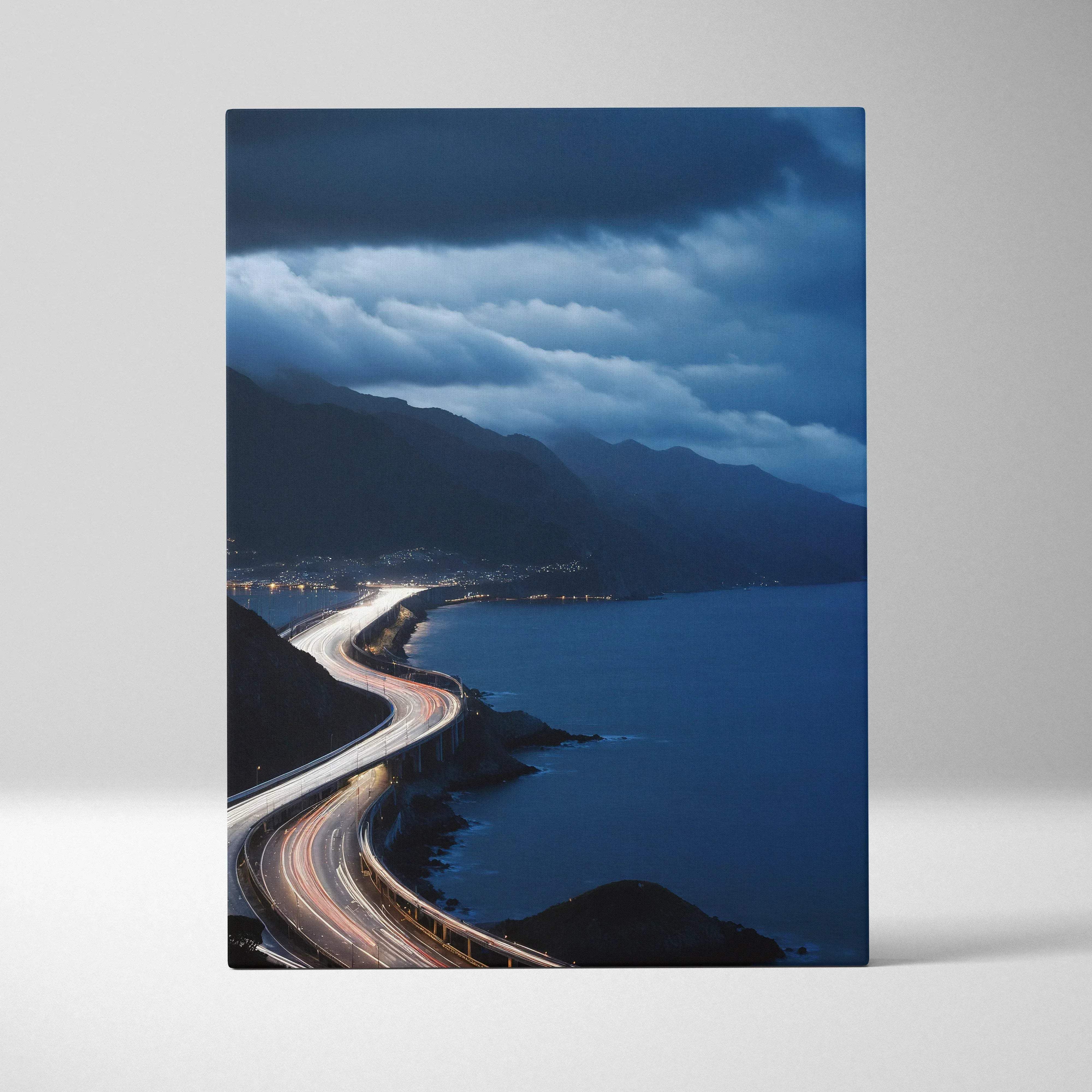 Rectangular canvas print showing a moody blue coastal highway at night with light trails by the sea through mountains