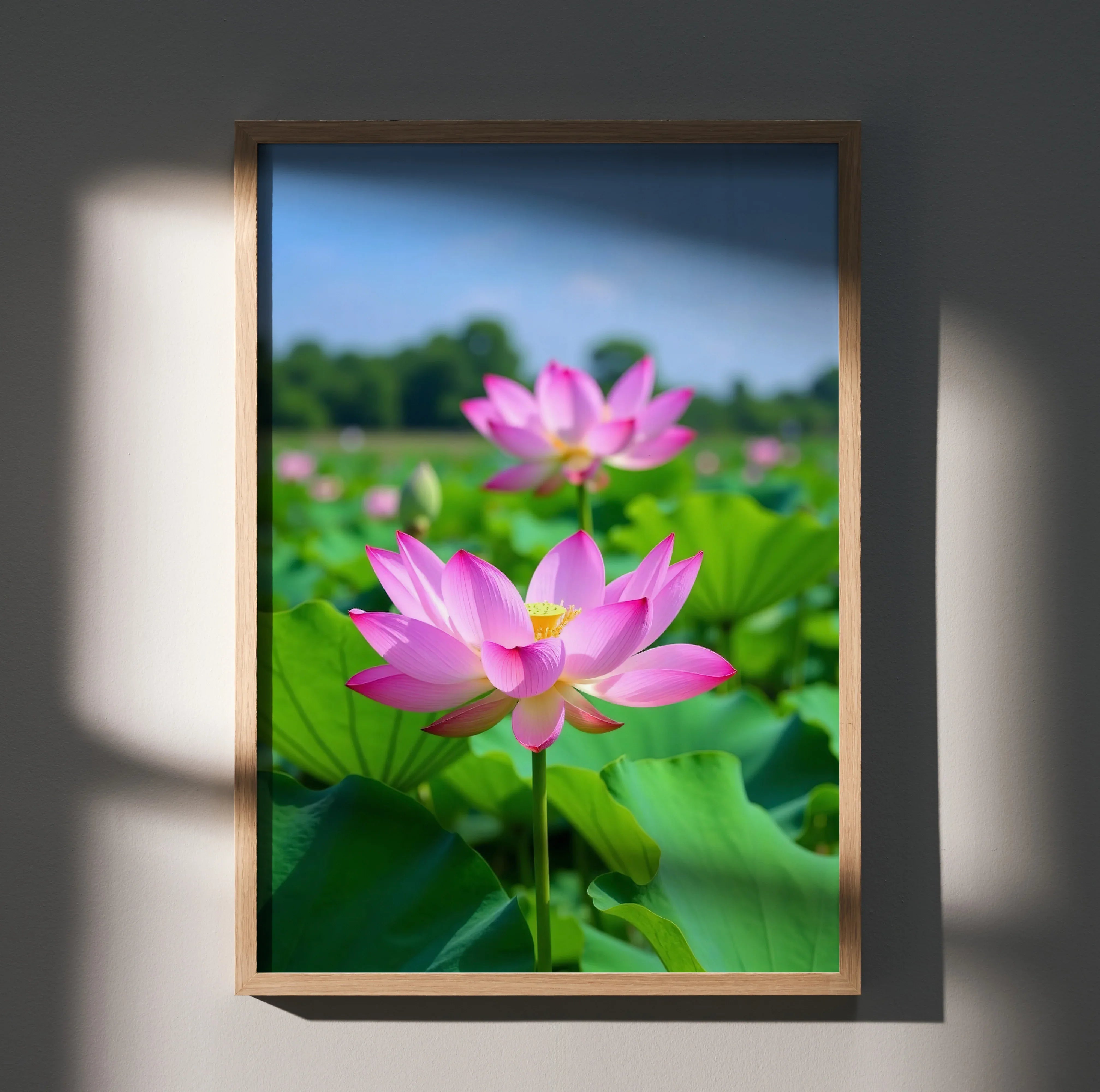 Vertical wall art poster featuring vibrant pink lotus flowers with green leaves against a blurred blue sky background.