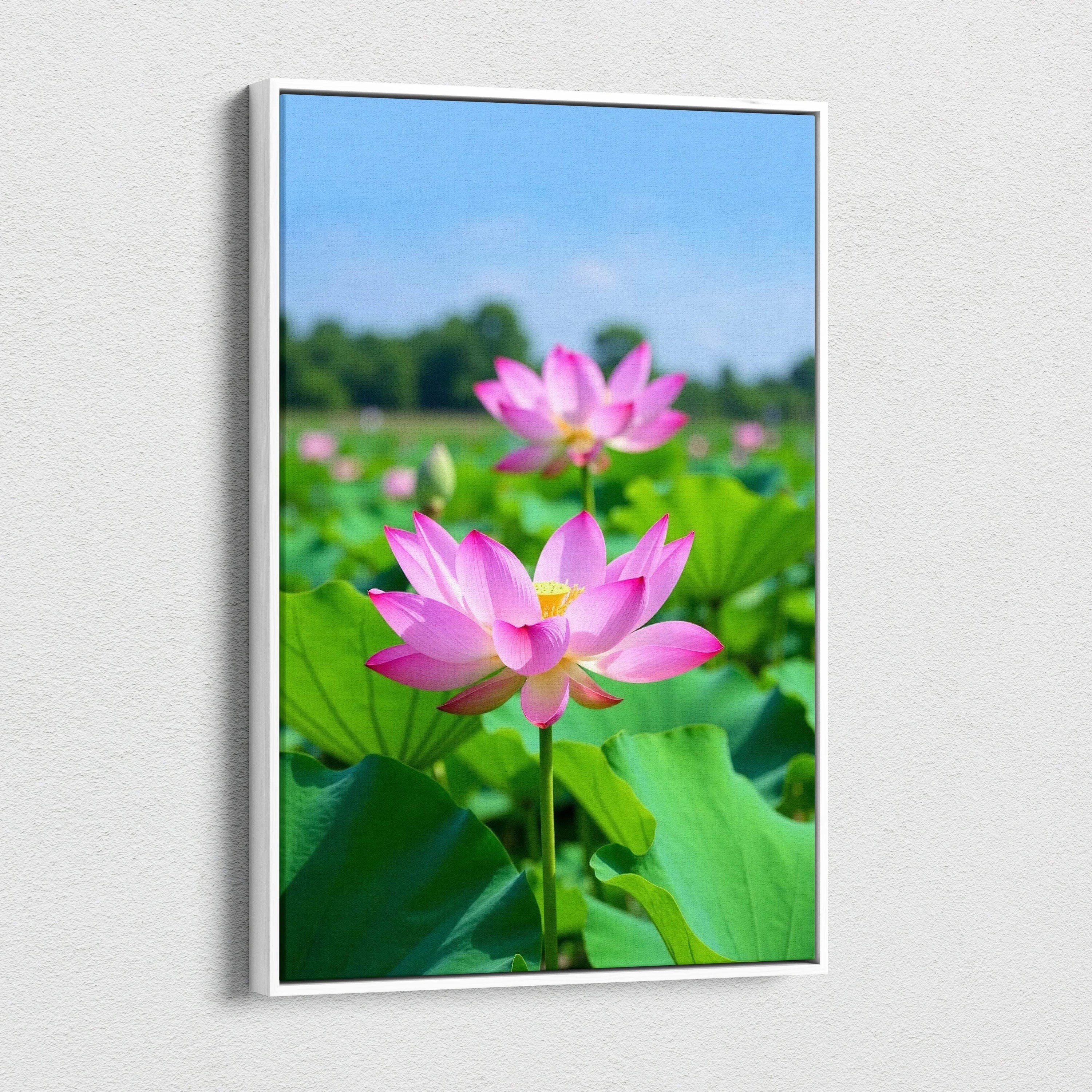 Vertical canvas wall art featuring vibrant pink lotus flowers with green leaves under clear blue sky.