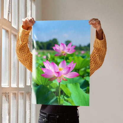 Vertical wall art poster with vibrant pink lotus flowers and green leaves against a blue sky background.